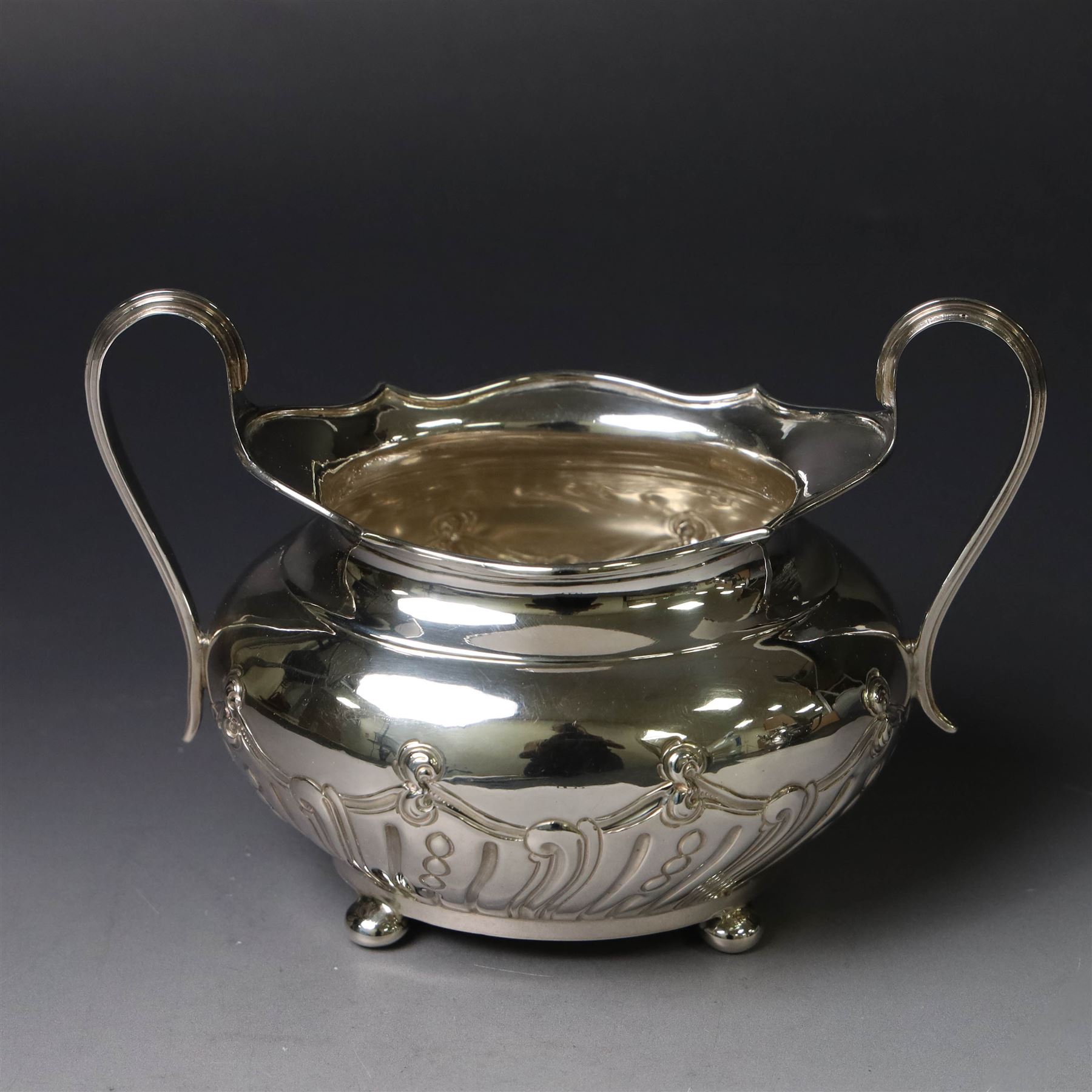 Edwardian silver three piece tea service, comprising teapot, twin handled open sucrier and a cream jug, each of oval form with embossed scrolling decoration and upon four bun feet, the teapot with ebonised wooden handle and finial, hallmarked Thomas Bradbury & Sons Ltd, Sheffield 1903, teapot H16cm