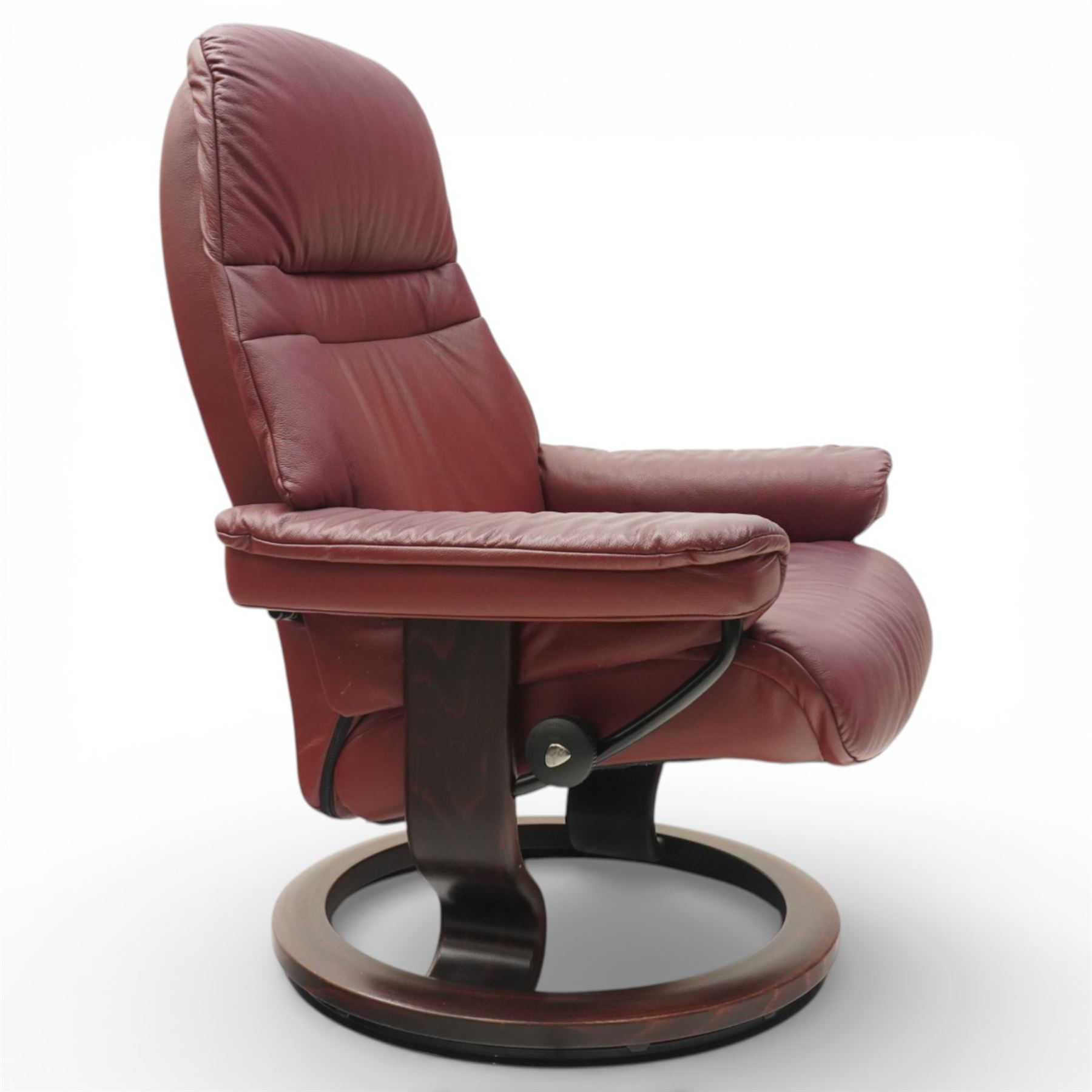 Ekornes - Stressless reclining armchair and matching footstool, upholstered in oxblood leather with padded headrest and segmented back cushion, shaped armrests with exposed adjustment handles, raised on stained laminated beech circular swivel base, the conforming stool on matching ring base
