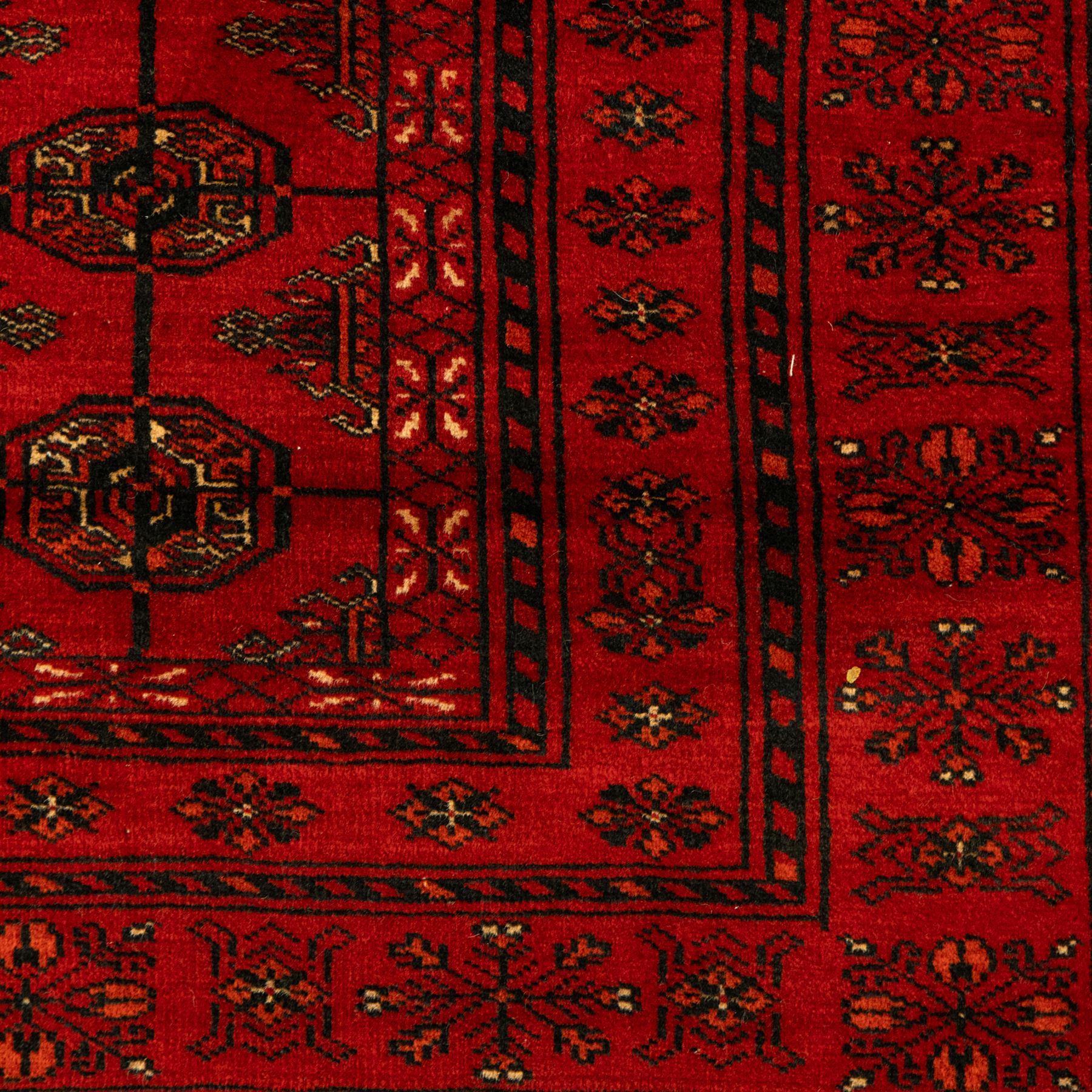 Turkman hand-knotted carpet, deep red ground, with an all-over field of repeating gul motifs arranged in rows, enclosed by multiple red geometric borders with stylised flowerheads and hooked motifs, flanked by narrow patterned guard stripes, with wool fringes