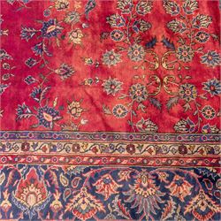 Large Persian-style mahal-type hand-knotted carpet, of rectangular form with a deep crimson field decorated with an all-over arrangement of stylized floral sprays and palmettes, with a central subtle medallion composition enclosed by a dark navy main border of scrolling floral motifs between narrow guard stripes with fringe ends 