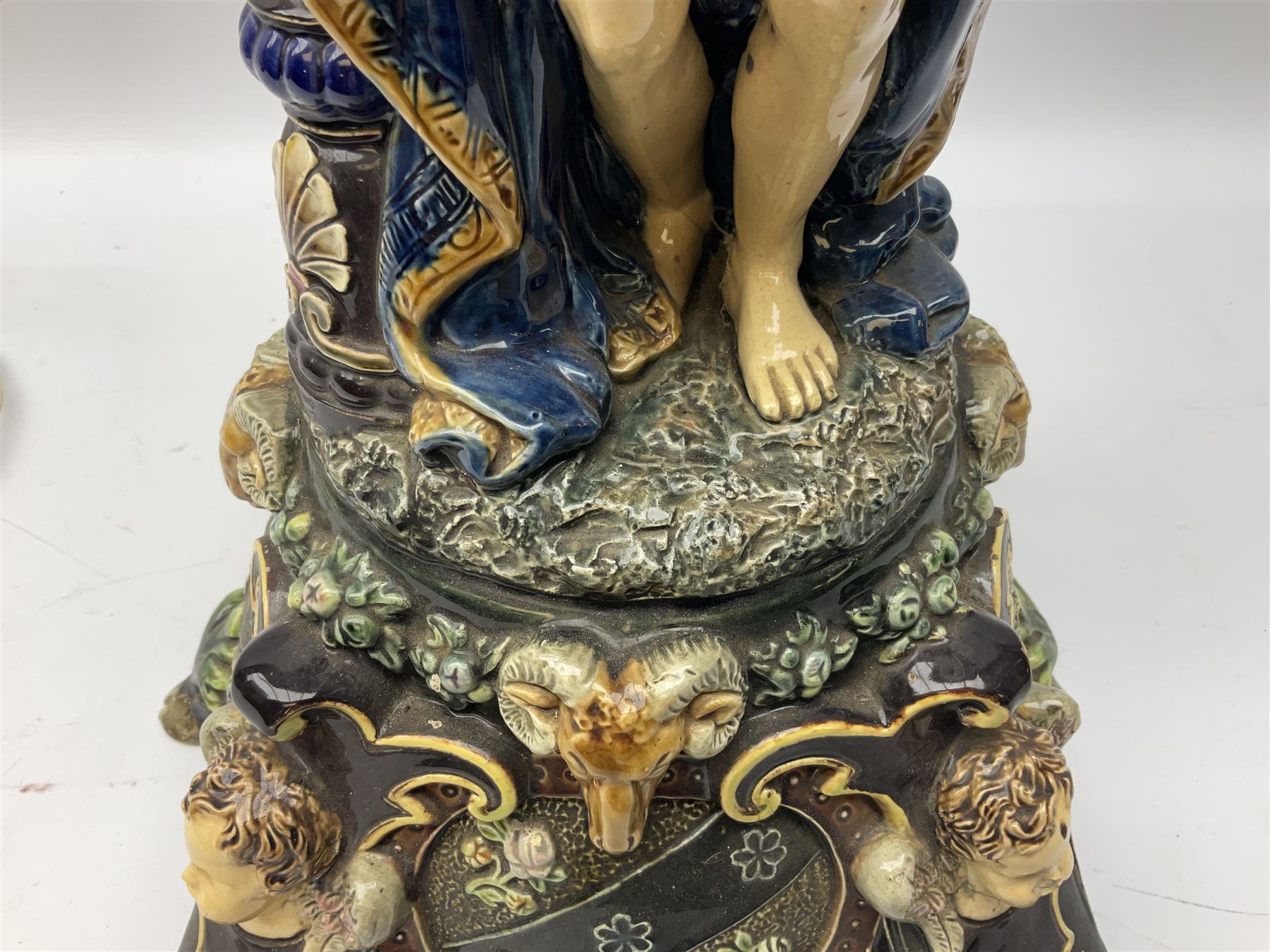 Composite table lamp modelled as a Roman Emperor donning blue robes, upon quatrefoil base modelled with rams heads and winged cherubs, H56cm excl fitting
