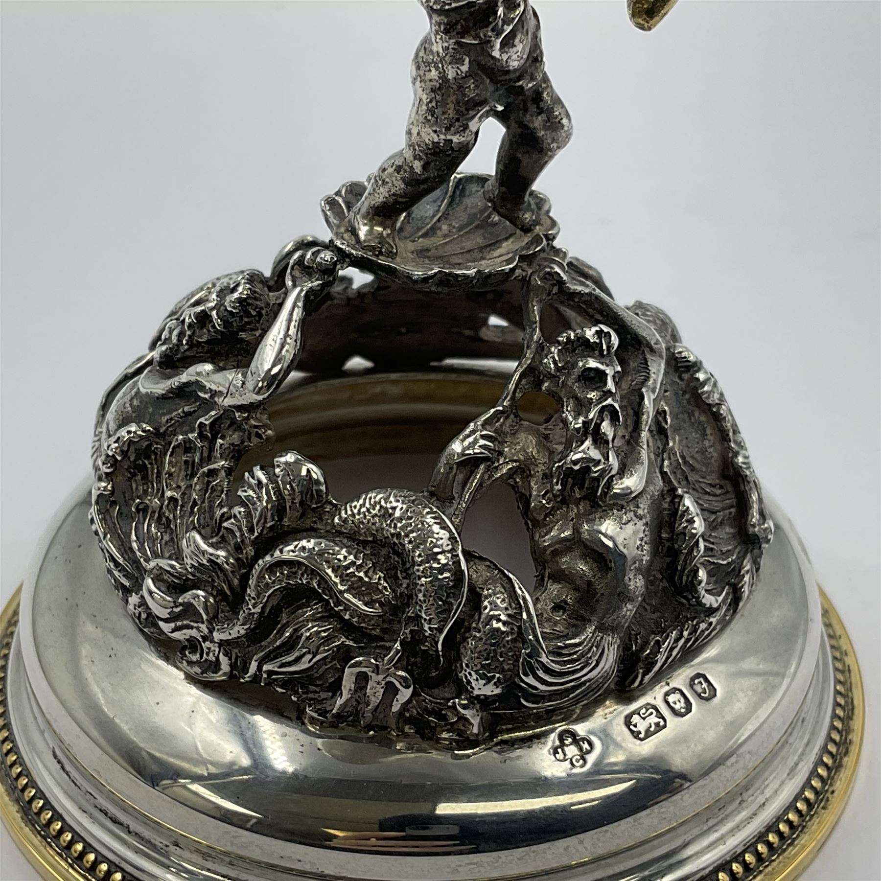 Modern limited edition silver mounted nautilus shell cup, no. 42/150, the pearlescent shell cup with silver-gilt strapwork to rim, upon a stem modelled as a putto supporting a gilt cornucopia and circular domed foot depicting Poseidon amongst swirling waves, hallmarked by St James House Company, London 1980,  H17.5cm