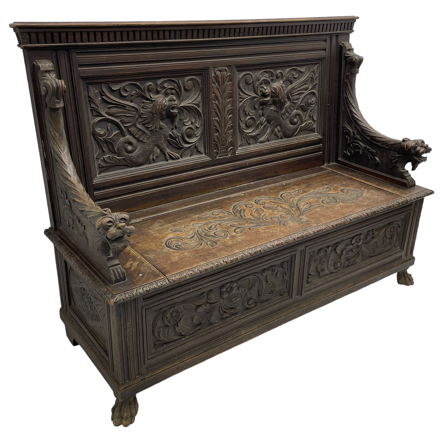 19th century oak hall bench, dentil cresting rail over moulded frame with panelled back carved with fire-breathing mythical beasts and central acanthus leaf motif, scroll carved down-sweeping arms carved with grotesque masks with scrolled foliage and shells, hinged box seat carved with scrolling foliage over panelled front with further carved foliage decoration, on paw carved front feet 