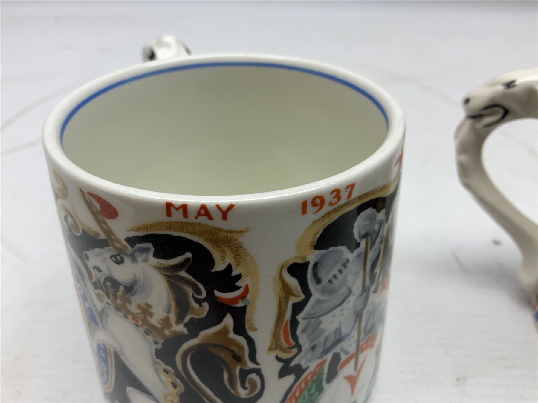 Two Dame Laura Knight coronation mugs for King George VI and Queen Elizabeth, comprising a Burleigh Ware example and a J&G Meakin example, each with a lion moulded handle and printed marks beneath, H8cm