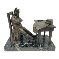 After E Carlier; a bronzed spelter desk stand as Napoleon seated with arms crossed at a table with maps, books and aperture for a lamp, on marble base with plaque entitled 