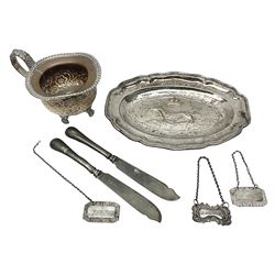 Silver plated tray, with shaped rim and embossed with a dog and crown to centre, stamped Valenti, together with three silver plated decanter labels, two port and one Bucellas, a plated cream jug with embossed floral decoration and a pair of plated fish knives engraved with double headed eagle to handle, tray W25.5