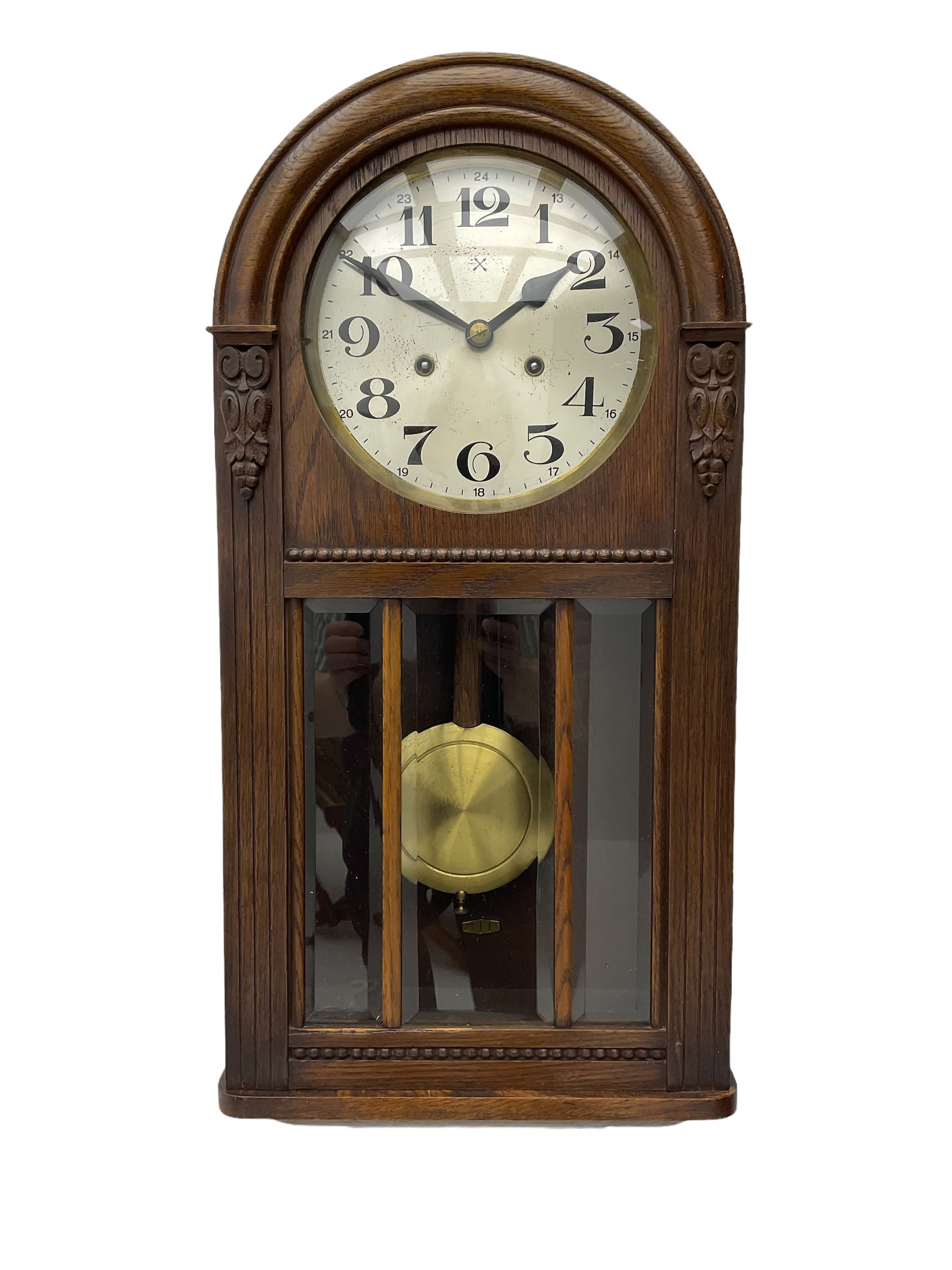 German HAC “ting tang” quarter striking wall clock in a round arched oak case with applied carving and beadwork, glazed door with a visible pendulum and silvered 24-hour dial with Arabic numerals and steel spade hands,  8-day spring driven movement striking on gong rods.

