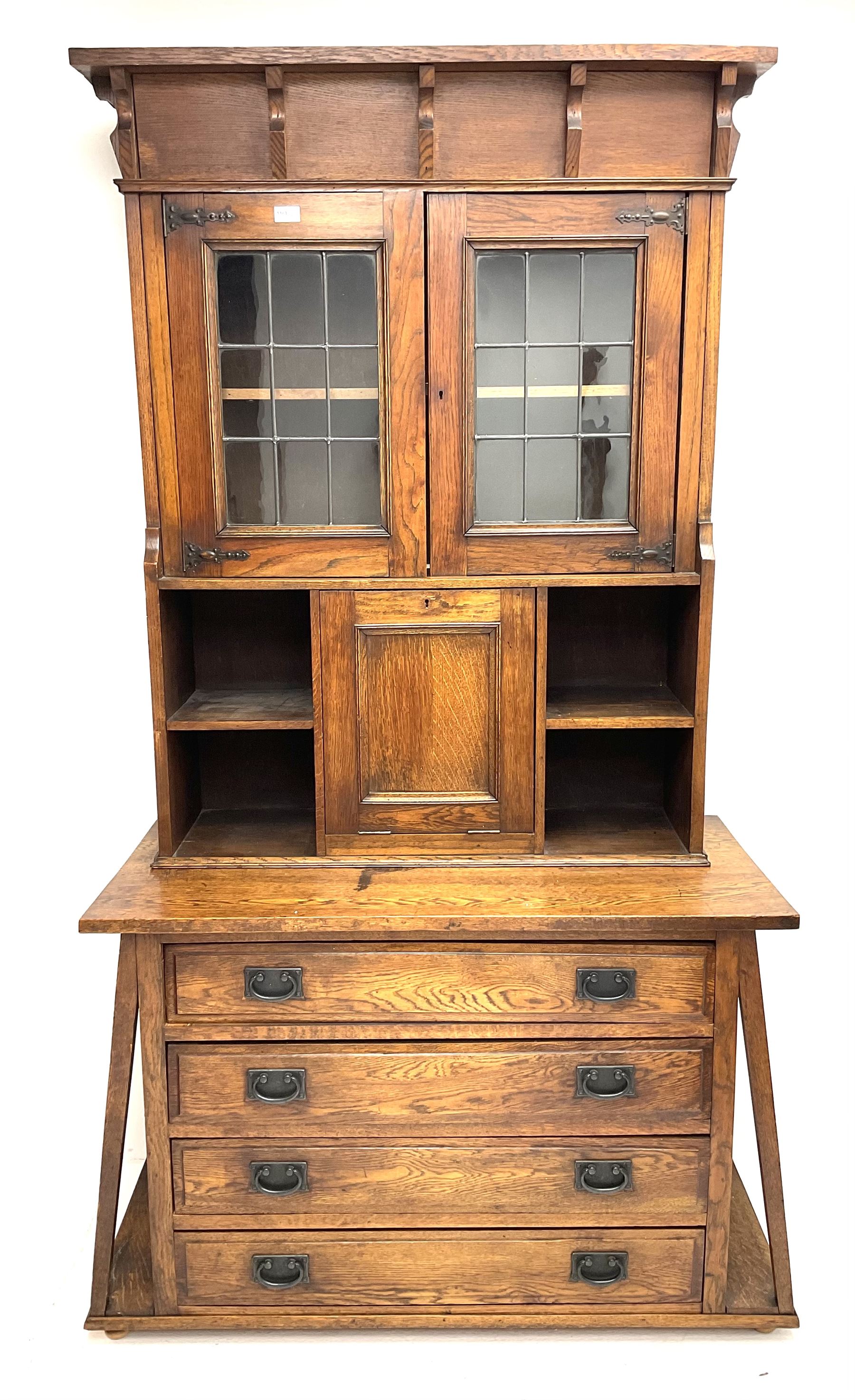 Arts & Crafts oak cabinet on chest, projecting cornice above to lead glazed cabinet doors, two shelves flanking single fall front enclosing fitted interior, four graduating drawers