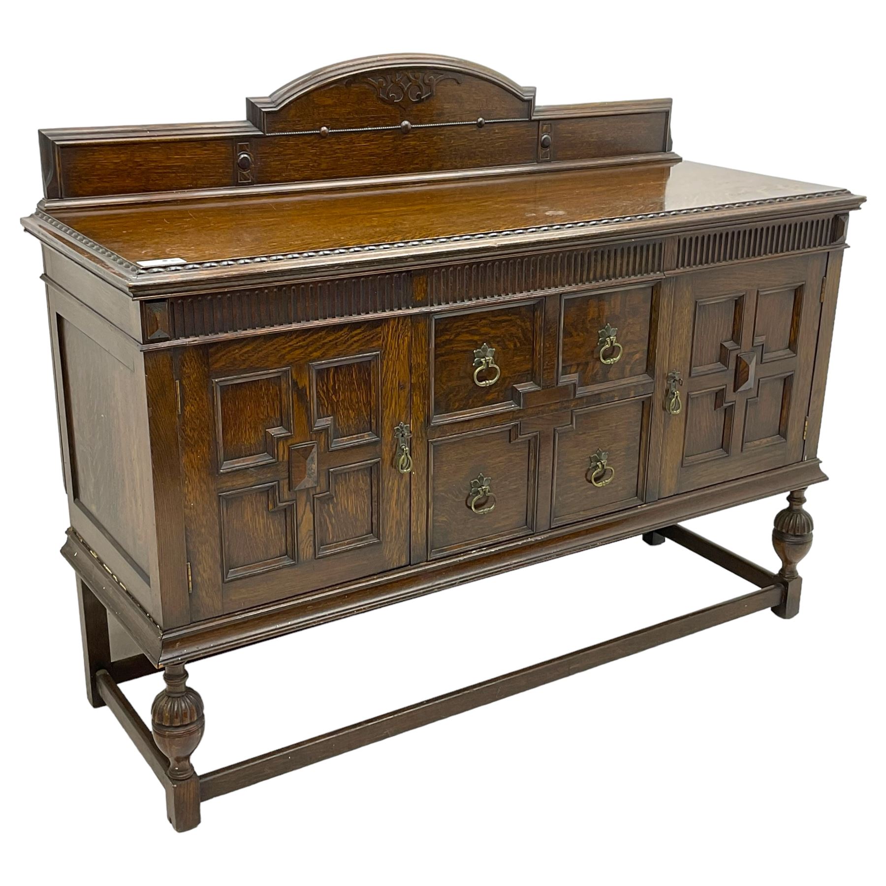 Early 20th century oak sideboard, raised stepped arch back over moulded rectangular top, fitted with two drawers and two panelled cupboards with geometric mouldings, on turned and lobe carved baluster feet united by stretchers 