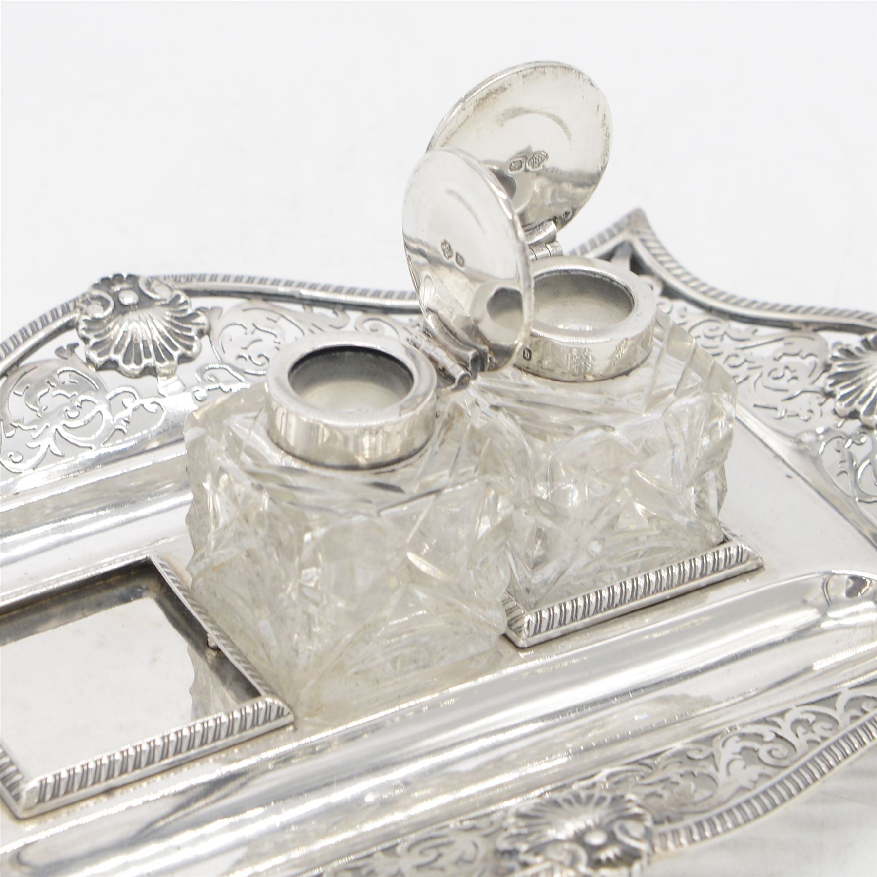 Late Victorian silver desk stand, of rectangular form, with shaped and pierced, oblique gadrooned rim, upon four paw feet, the central tray with two pen holders and two reserves holding cut glass silver topped inkwells, hallmarked William Hutton & Sons Ltd, Sheffield 1900, tray W23cm