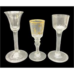 Three 18th century wine glasses comprising a plain stemmed glass with bell shaped bowl and conical folded foot H16cm, another plain stemmed glass with ogee bowl and folded foot and a Continental glass with gilt faceted bowl, decorated with male figure within a landscape, on a clear Silesian seven sided cut stem (3)