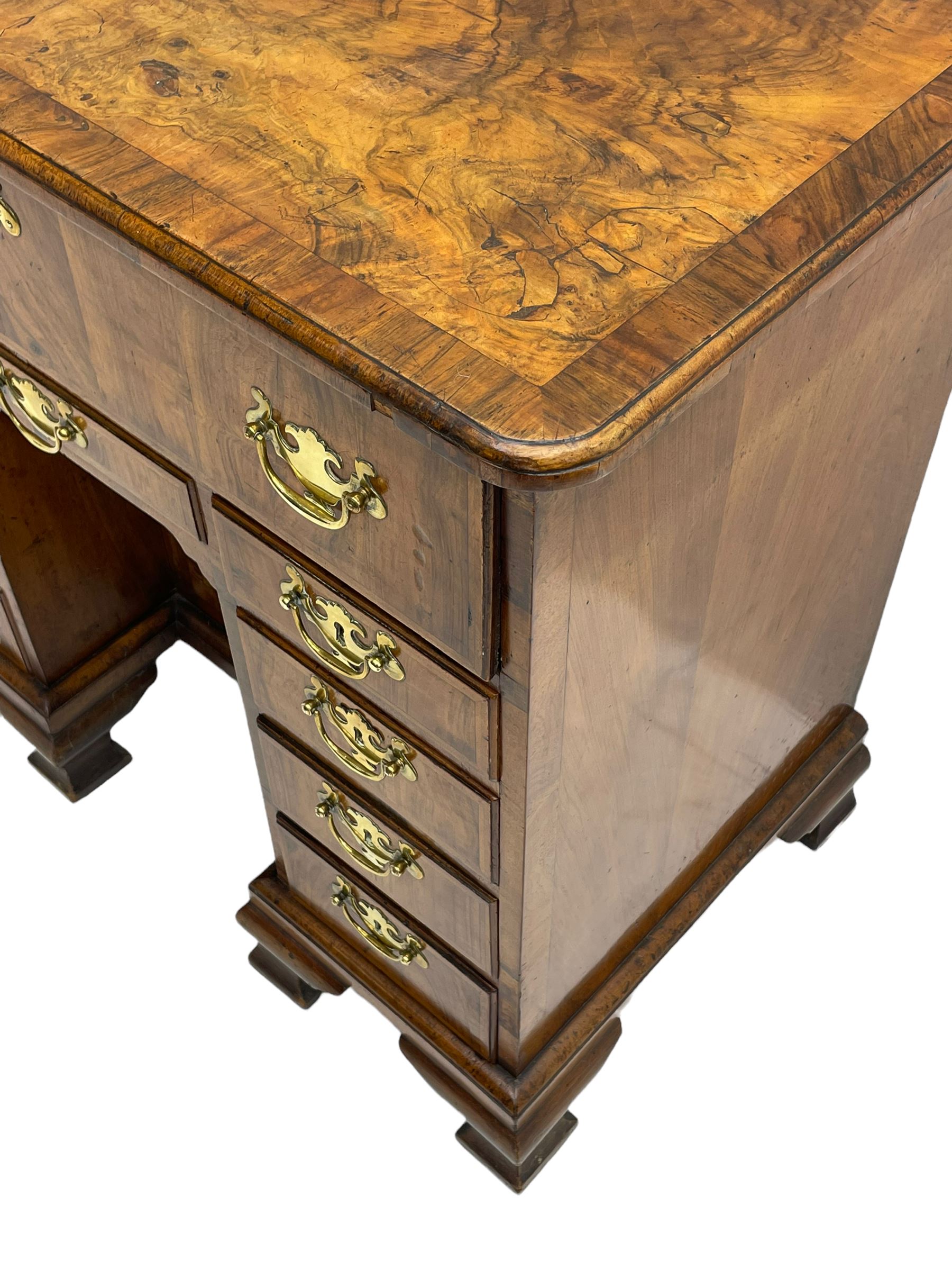 Early 18th century Queen Anne figured walnut kneehole desk with secretaire drawer, moulded and book matched top with walnut band, the top drawer with fall front enclosing small drawers and pigeon holes, fitted with nine drawers and central recessed cupboard, on ogee bracket feet