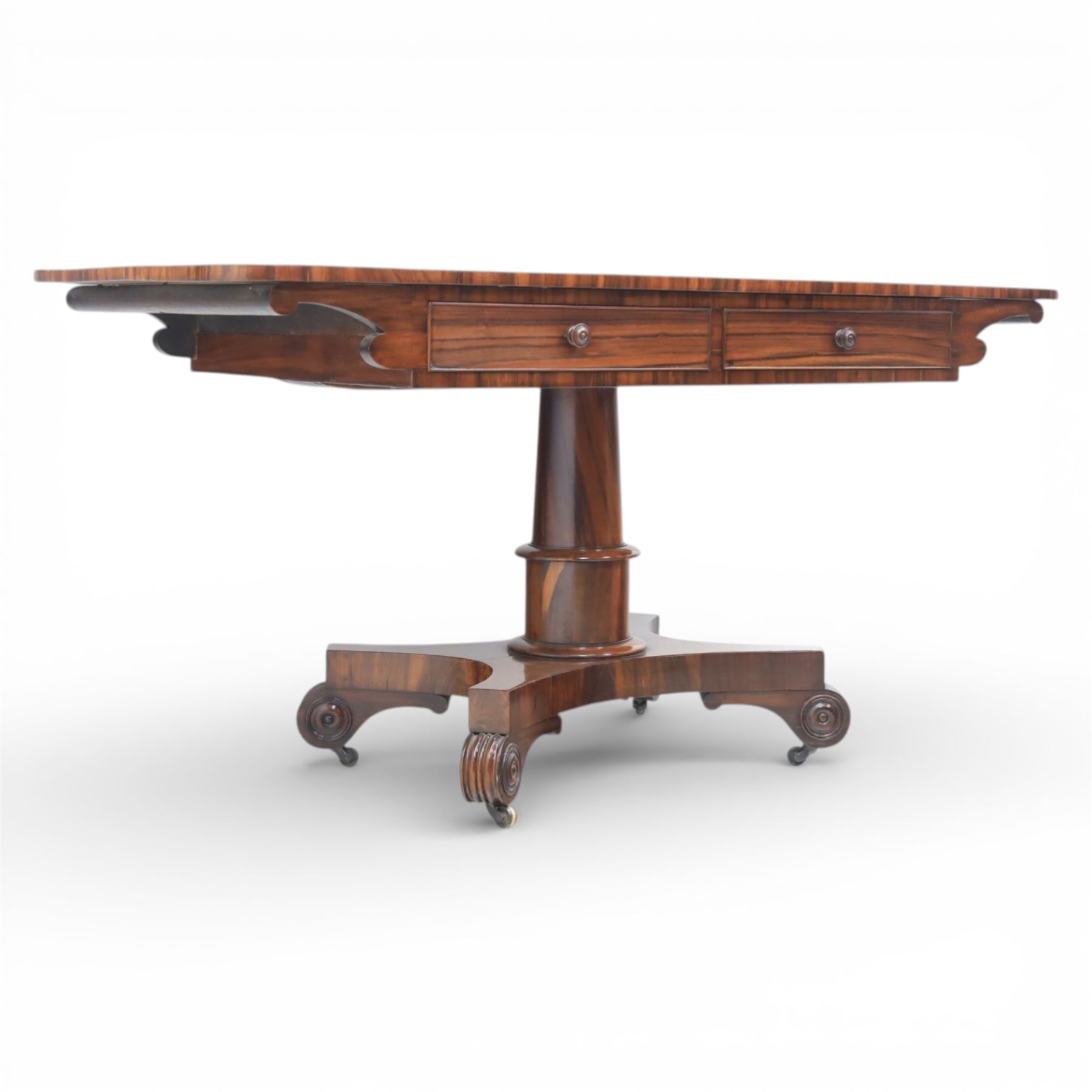 Victorian rosewood library table, rounded rectangular top with two frieze drawers with turned wooden knobs, quatriform base with scrolled ends terminating in brass castors  