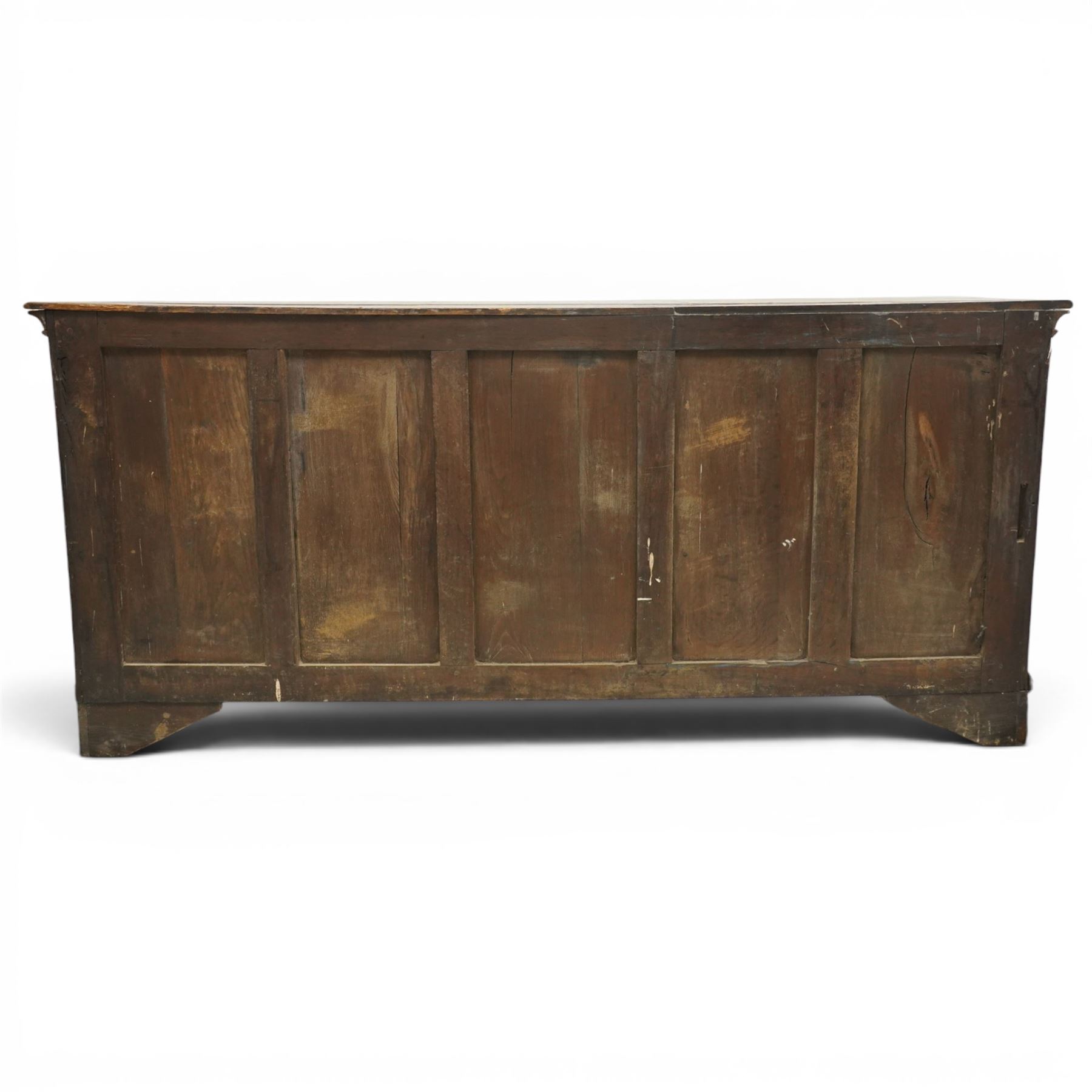 19th century Georgian oak long dresser base, rectangular plank top above a central frieze drawer over a fielded panel cupboard, flanked by three banks with quarter cantered pilasters, brass swan neck handles and escutcheons, raised on shaped bracket feet