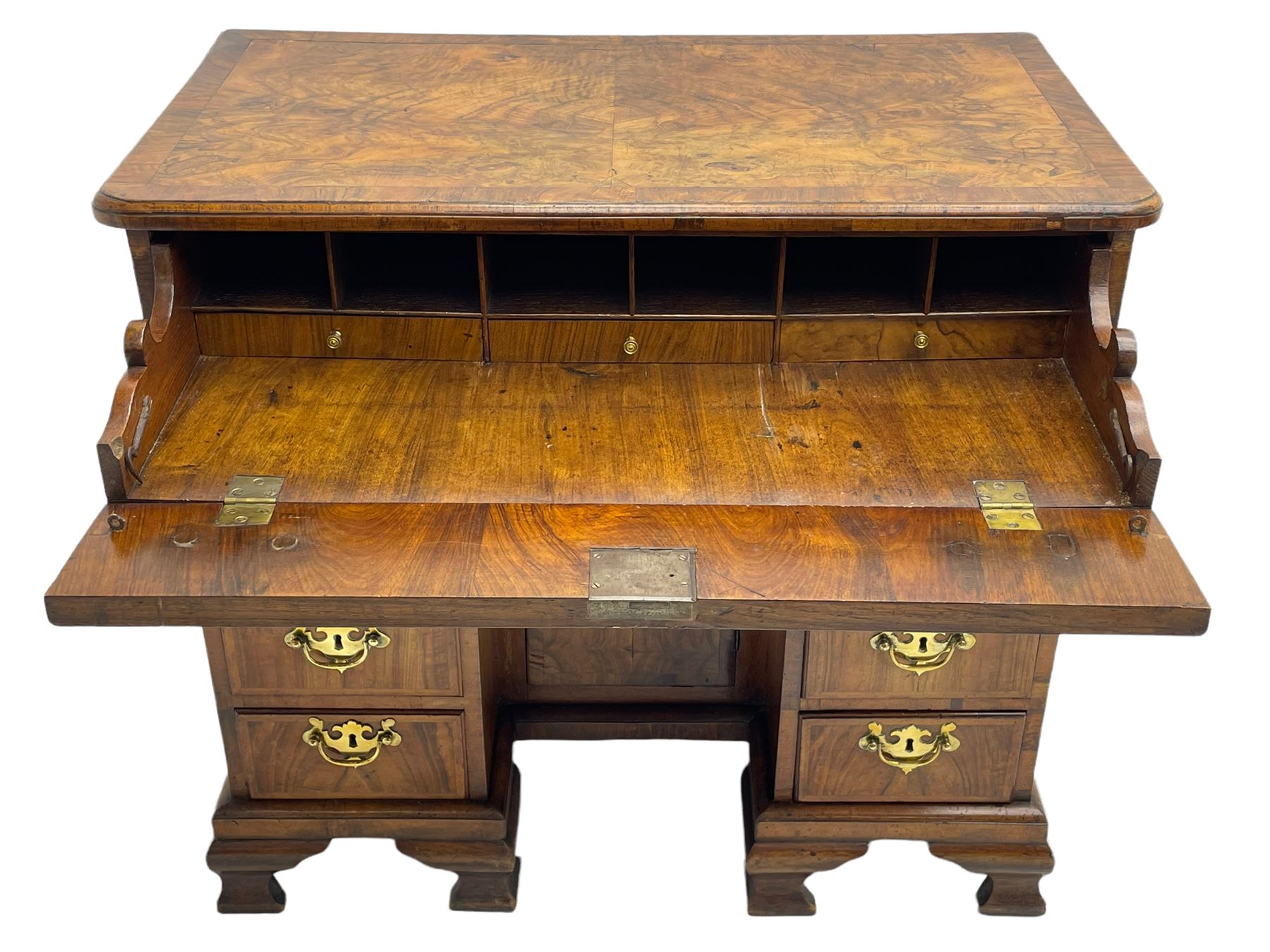 Early 18th century Queen Anne figured walnut kneehole desk with secretaire drawer, moulded and book matched top with walnut band, the top drawer with fall front enclosing small drawers and pigeon holes, fitted with nine drawers and central recessed cupboard, on ogee bracket feet