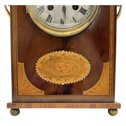 Edwardian- 8-day mantle clock in a mahogany case with a serpentine top and contrasting inlayed panels in satinwood and boxwood to the front, on a rectangular plinth raised on ball feet, silvered dial with Roman numerals and steel spade hands, twin train Parisian rack striking movement, sounding the hours and half hours on a coiled gong. With pendulum.