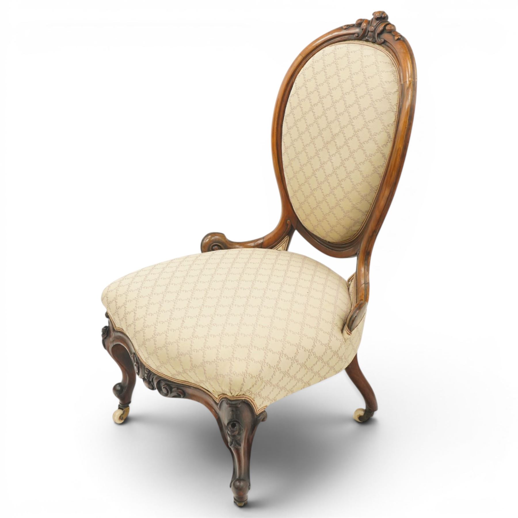Pair of Victorian walnut framed ladies salon nursing chairs, oval cameo back with carved cartouche carved cresting rail, sprung seat upholstered in foliate patterned ivory fabric, shaped apron carved with scroll and cartouche decoration, on cabriole supports with moulded flower knees, retailed by David Hick Interiors, Jersey