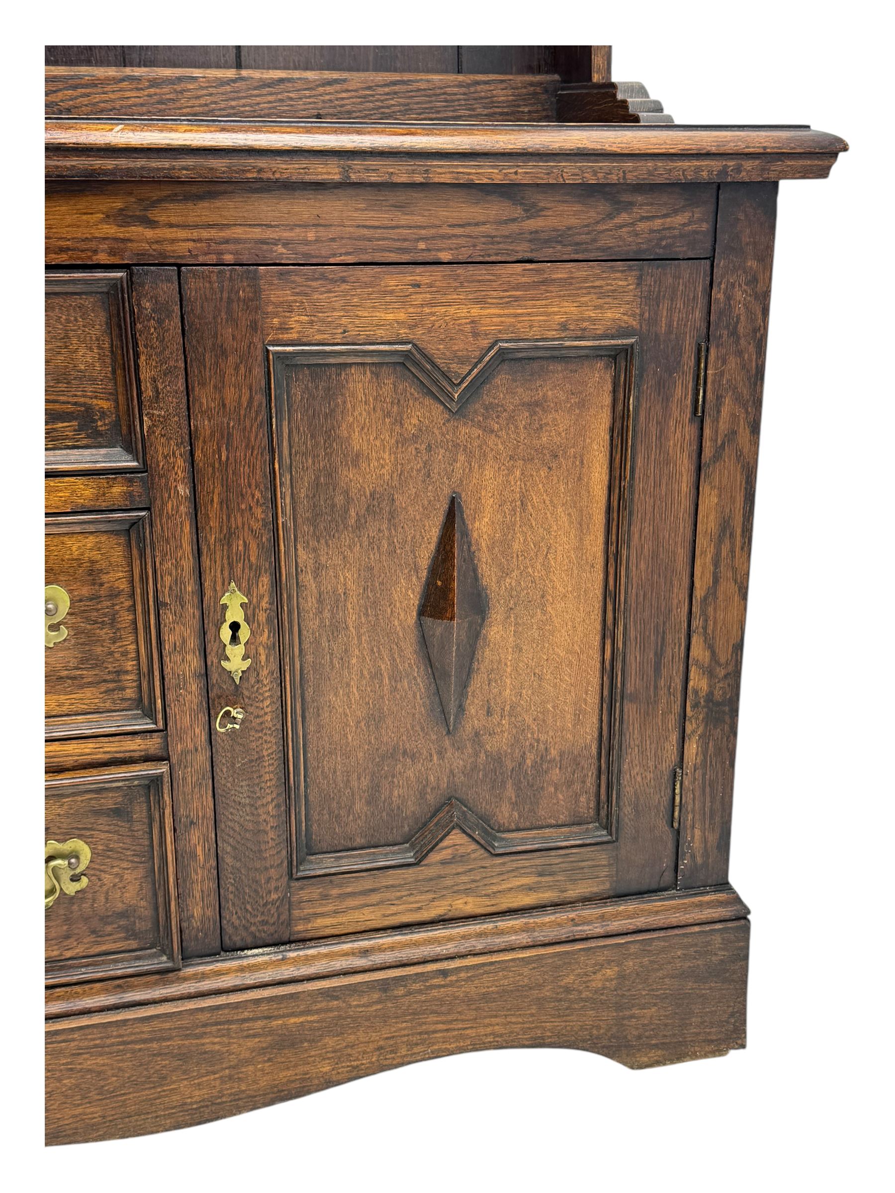 Late 19th century oak dresser, the upper section with two shelves beneath a shaped cornice, the lower section with a central bank of three drawers flanked by cupboard doors, all decorated with geometric diamond motifs, the drawers fitted with brass handles, raised on a shaped plinth base