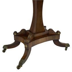 Regency rosewood and brass inlaid card table, the rectangular fold-over and swivelling top with rounded corners with a satinwood band, opening to reveal a blue baize lined interior playing surface, the frieze with a raised panel with satinwood stringing and a lower beaded brass edge, the concave and canted column with a shaped platform base applied with scrolls with brass star inlays and stringing, quadruple splayed supports terminating in foliate cast cups and castors