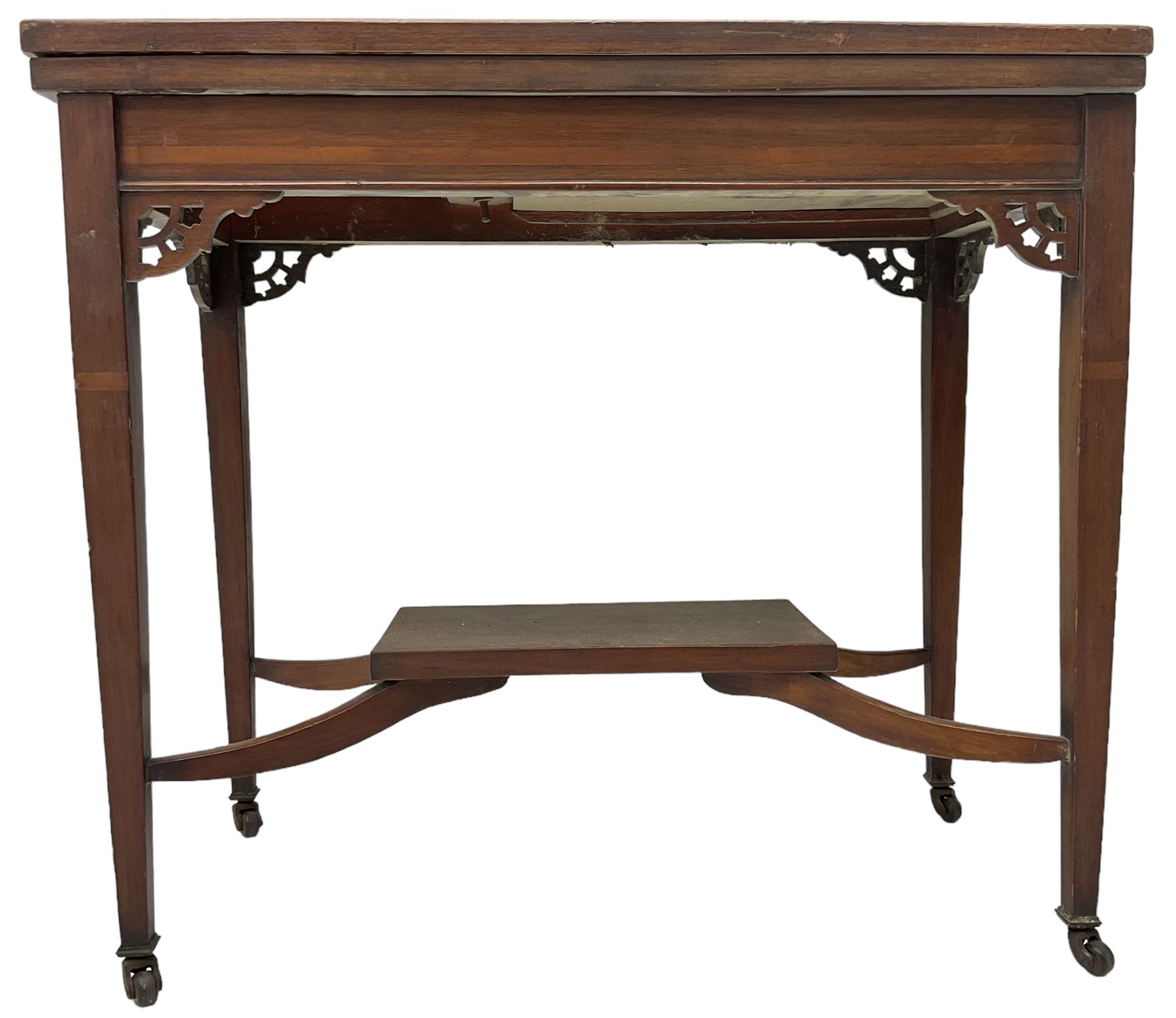 Edwardian inlaid mahogany games table, the rectangular fold-over swivel top decorated with central shell motif inlay and ebony stringing, raised on tapering supports united by shaped X-stretcher and undertier