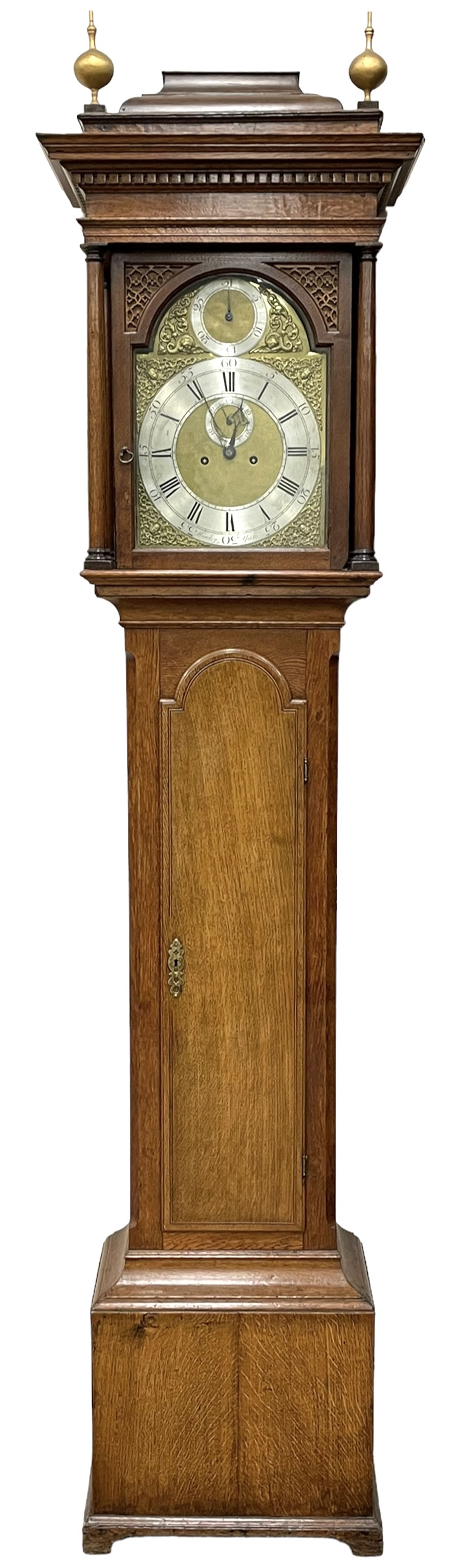 Henry Hindley of York – mid-18th century oak cased 8-day longcase clock,
flat topped caddy pediment with gesso finials, rectangular hood door flanked by wooden turned pilasters with capitals, canted trunk with a full-length break arch topped door on a short plinth with applied skirting and bracket feet, brass dial with a silvered chapter ring, Roman numerals and five-minute Arabic’s, minute and inner quarter hour tracks, matted dial centre with subsidiary seconds dial, blued steel hands and female head pattern spandrels, silvered calendar dial to the break arch with dolphin spandrels, four pillar rack striking movement, striking the hours on a bell. With weights and pendulum. 
H250 W48 D27
Henry Hindley originally from Wigan (Lancs) is recorded as working in York from Petergate 1731-41 then Stonegate 1741-1771. A famous and highly innovative maker, often referred to as the “Tompion of the North.” 
