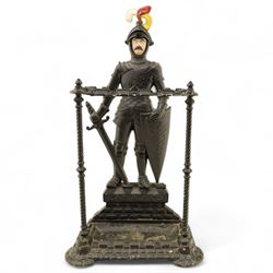 Early 20th century painted cast iron hall stand, formed as a standing armoured figure with red and yellow feathered crest, twin rails and integral drip tray with castellated edge