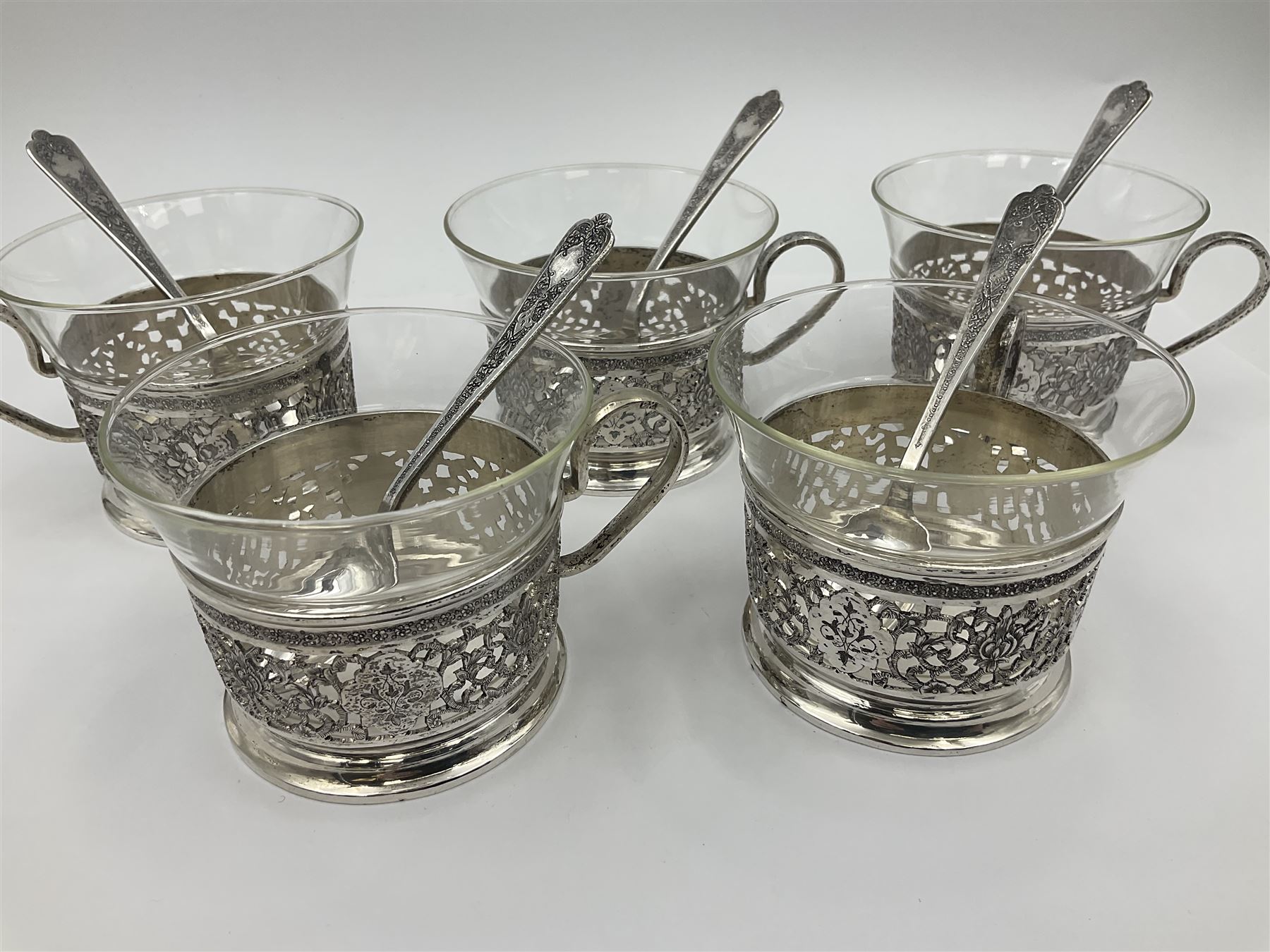Early/mid 20th century Persian silver tea service, comprising circular serving tray, teapot, twin handled sucrier and cover, milk jug, five tea glasses with six silver holders, six tea spoons, and pair of sugar tongs, each profusely chased with foliate arabesque decoration, each bearing marks including 84 for 840 fineness, tray D40cm, teapot H16cm