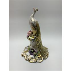 A Royal Crown Derby porcelain figure, modelled as a peacock perched upon an urn of encrusted flowers, upon a scrolling base with scrolling gilt and encrusted flower decoration, with printed mark beneath, with makers box, H24cm. 