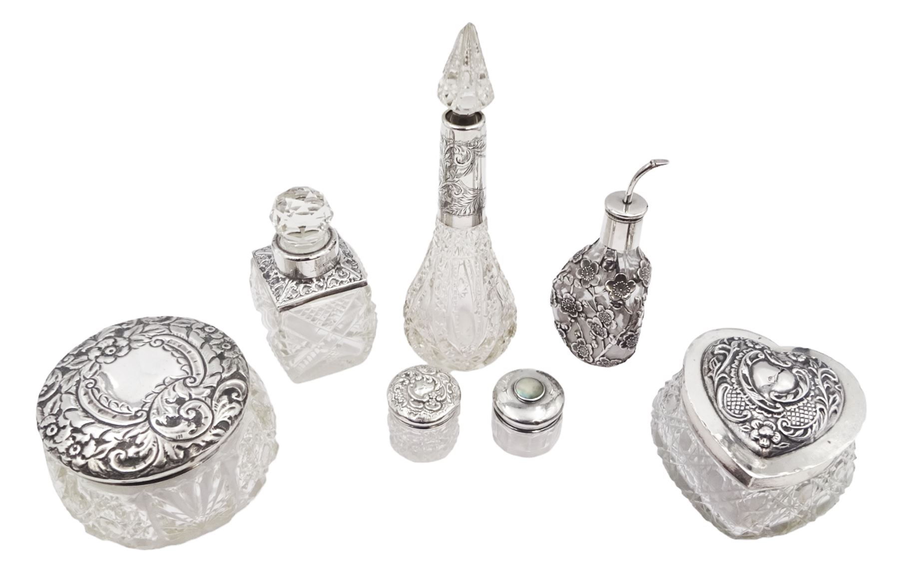 Two silver mounted dressing table jars, one in the form of a heart, both with embossed silver covers and cut glass bodies, hallmarked, together with two smaller examples, one set with mother of pearl, three silver mounted glass scent bottles, including an example with prunus blossom decoration, stamped Sterling, tallest bottle H17cm