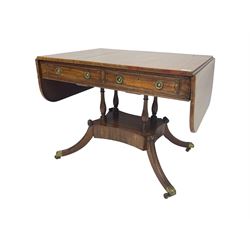 Regency period mahogany drop-leaf sofa table, rectangular top fitted with two cockbeaded drawers with ebony stringing, raised on turned columns united by quadrupod base, the sabre supports terminating in brass cups and castors