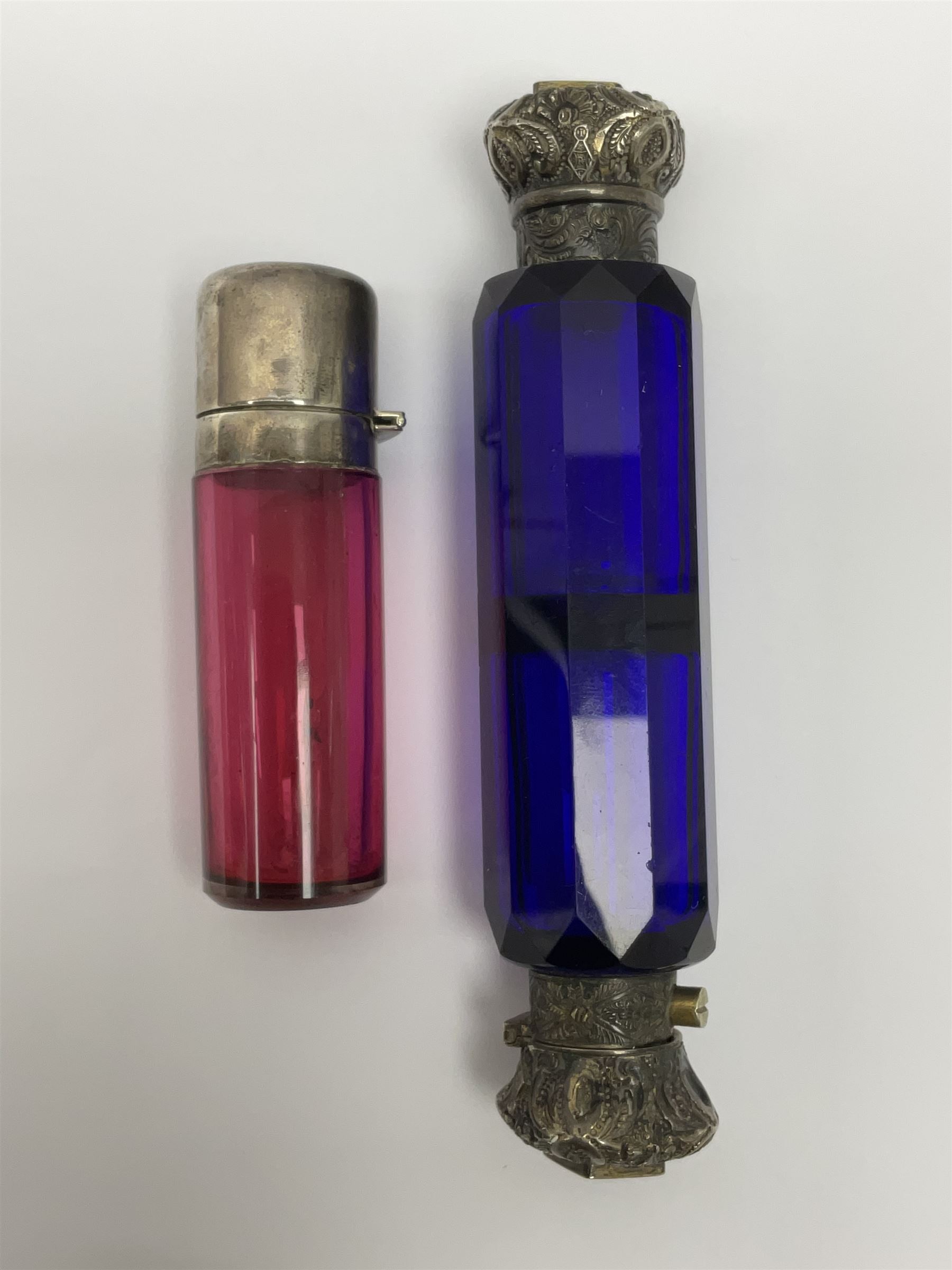 Late Victorian silver mounted ruby glass cylindrical scent bottle, with interior glass stopper, Birmingham 1900, makers mark worn, H8cm, together with a Victorian double ended cut blue glass perfume bottle mounted with white metal screw and flip caps decorated with foliate repousse detailing, H13.5cm