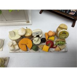 Collection of miniature dolls house grocery shop furniture and produce, comprising glazed corner counter with brass style cash register, shelved preserves unit, pies, cheese board and trays of meats, pair of white cheese counters, biscuit display with six tins, glazed preserves cabinet, pair of shop chairs and four further cheese boards complete with grapes and label flags