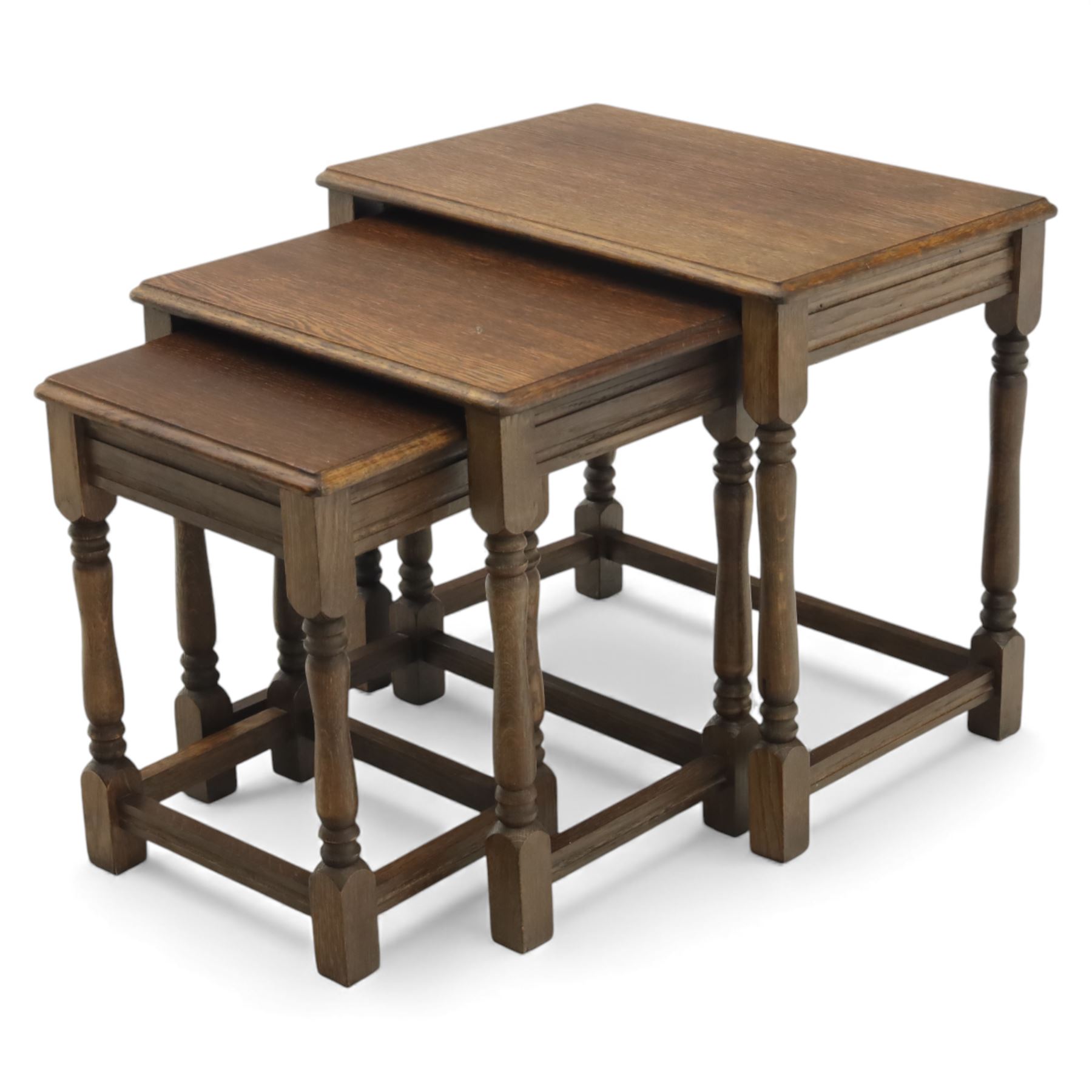 Nest of three dark oak tables, rectangular top with turned supports, tables suspended on rails