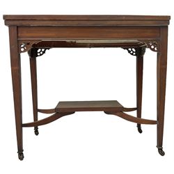 Edwardian inlaid mahogany games table, the rectangular fold-over swivel top decorated with central shell motif inlay and ebony stringing, raised on tapering supports united by shaped X-stretcher and undertier