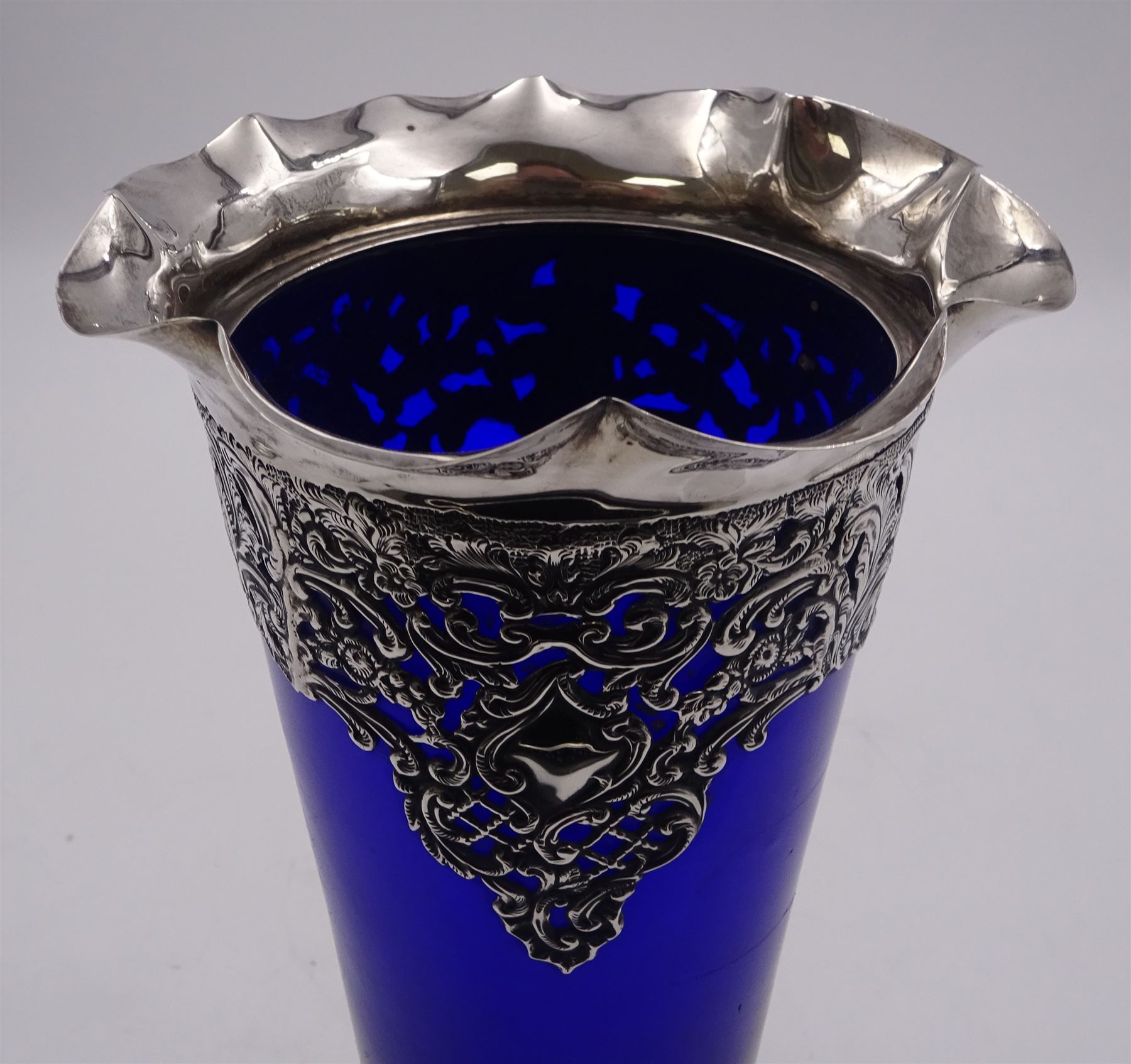 Victorian silver mounted blue glass trumpet vase, the silver mounts with pierced and embossed floral, C scroll and lattice decoration, with frilled rim, upon stepped circular foot, hallmarked Henry Matthews, Birmingham 1899