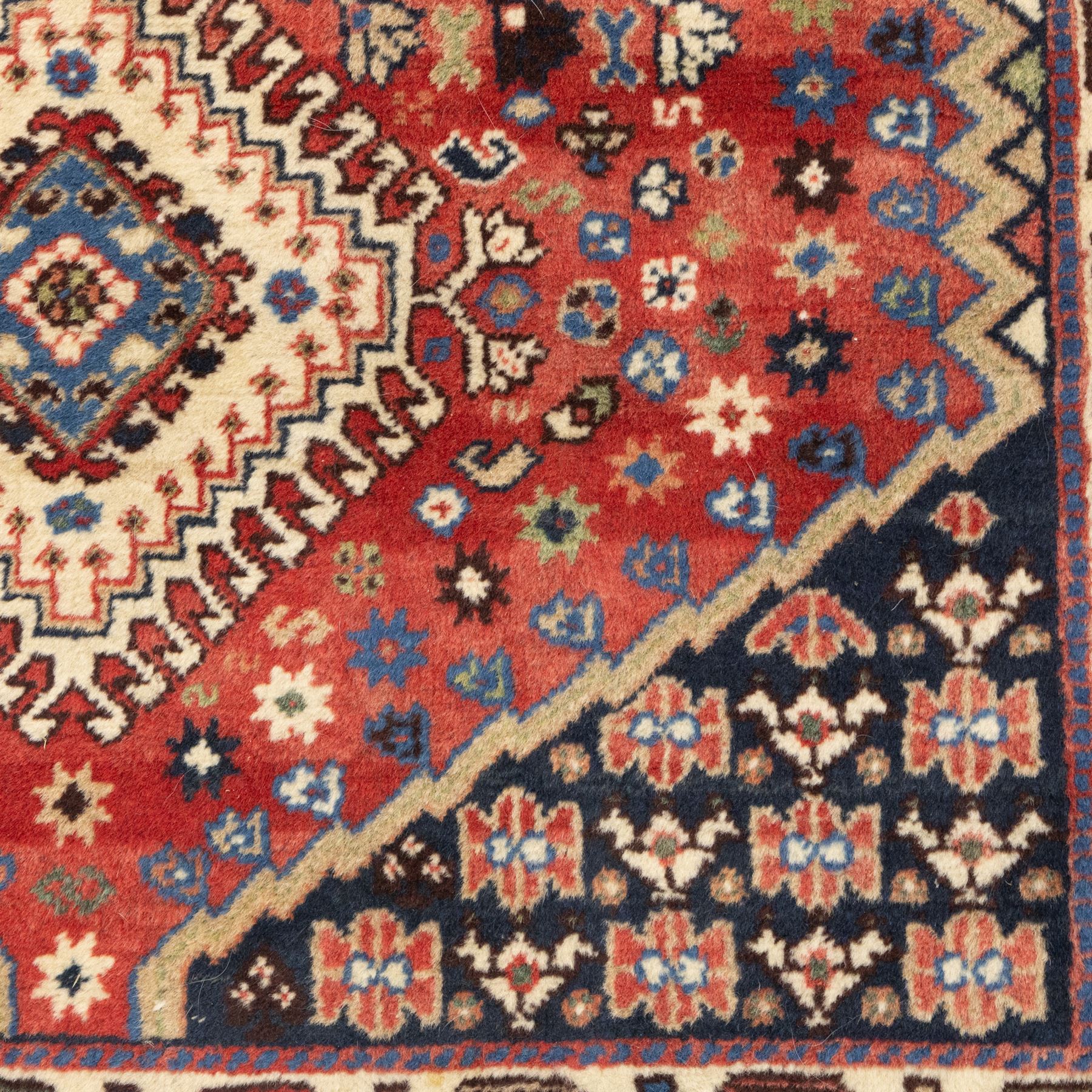 Persian Shiraz rug, wool on cotton foundation, with central row of linked diamond medallions in ivory, indigo and madder tones, stylised rosettes and angular vine motifs throughout, framed by a geometric border