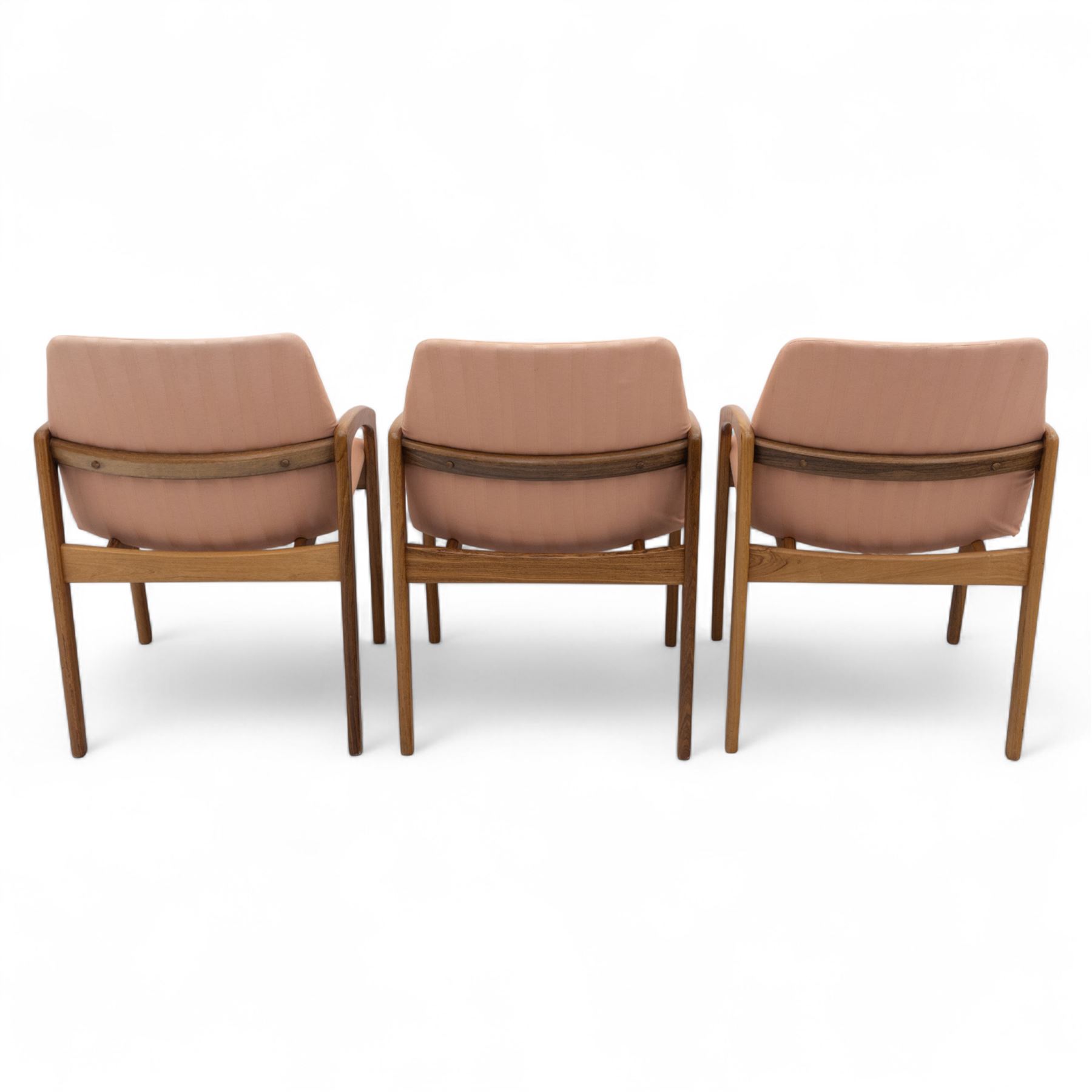 Mid-20th century Danish teak armchairs, each with curved open arms and upholstered seat and backrest in salmon pink striped fabric, raised on tapering legs