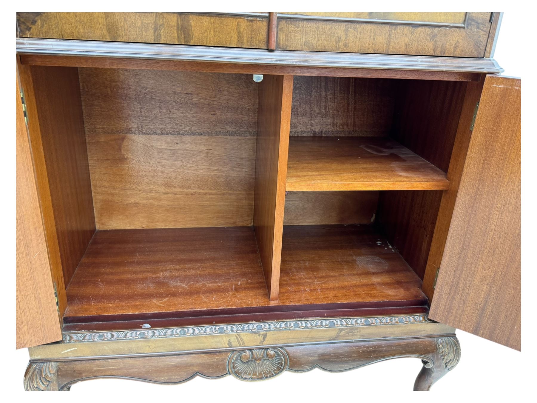 Early 20th century walnut veneered cocktail cabinet, shaped and carved foliate pediment above a pair of arched panelled doors with figured veneers and ornate cast escutcheons, interior is mirrored on the base and back, slide out mirrored shelf, flanked by foliate carved uprights, over a conforming lower cabinet, all raised on shaped apron and scroll carved cabriole feet