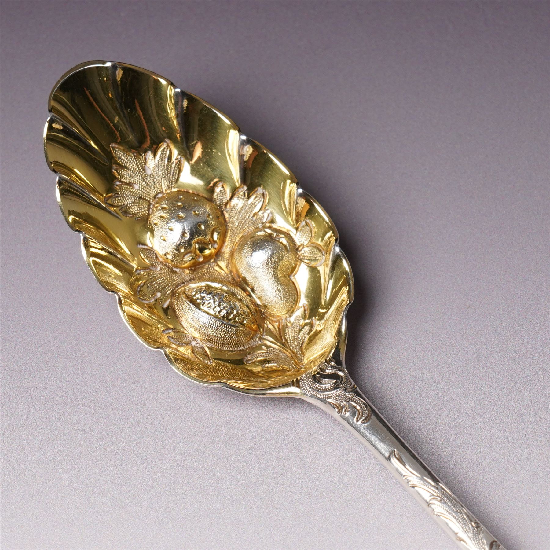 George III silver 'berry' spoon with later embossed and gilded bowl and engraved stem London 1786, sifting spoon similarly gilded and decorated and a George III silver fiddle and thread pattern table spoon London 1810 (3)