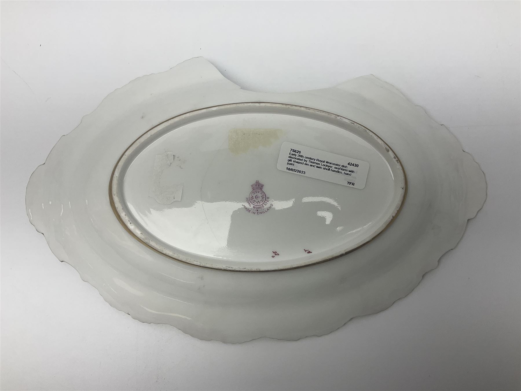 Early 20th century Royal Worcester dish decorated by Thomas Lockyer, oval form with gilt shaped rim and twin shell handles, hand painted with a still life of fruit upon a mossy ground, signed T Lockyer, with puce printed mark beneath and date code for 1922, for restoration, W31cm