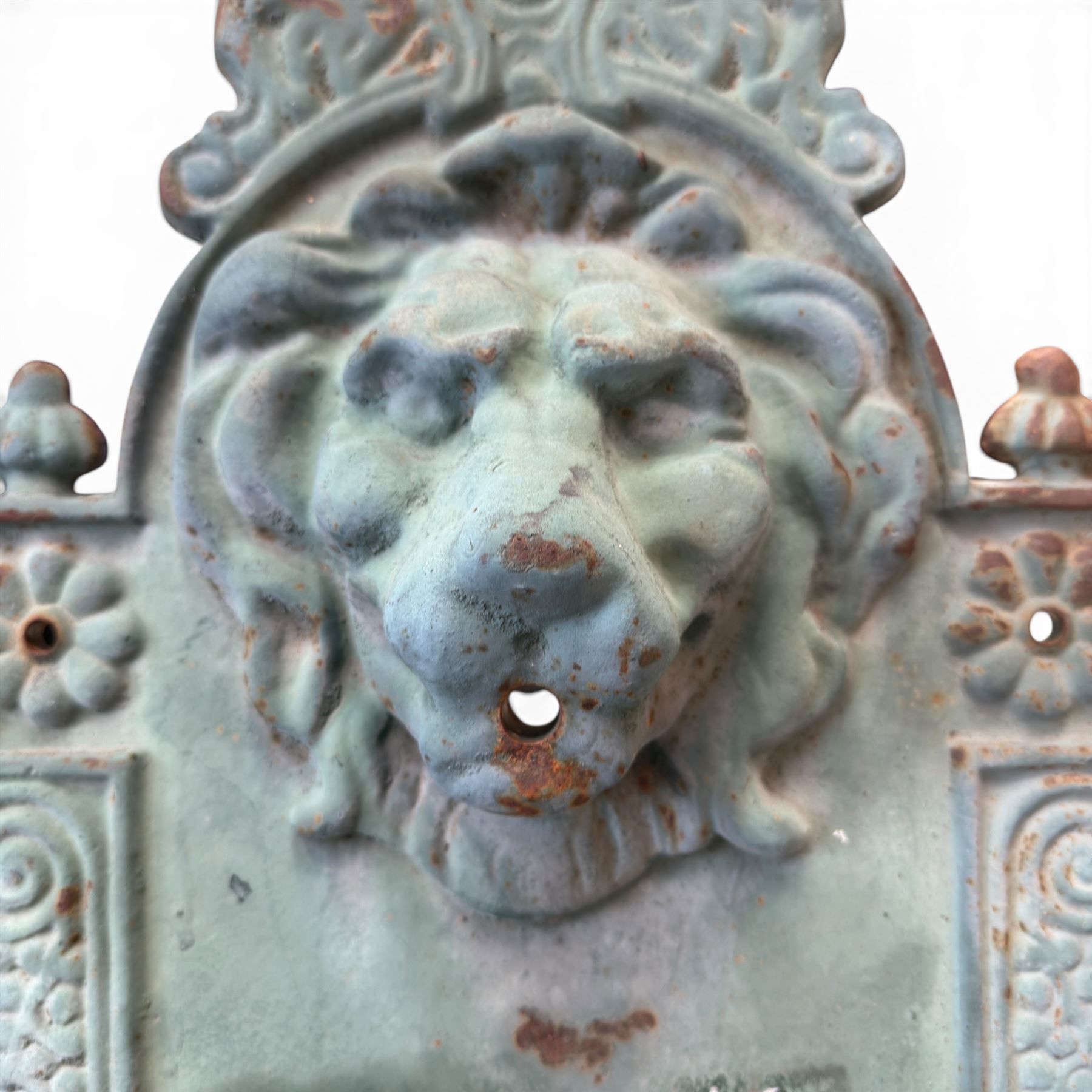 Antique cast iron wall fountain, cartouche cresting rail over a lion mask spout, with scroll and floral decoration over a scalloped basin, in rustic turquoise painted finish with rusted patina