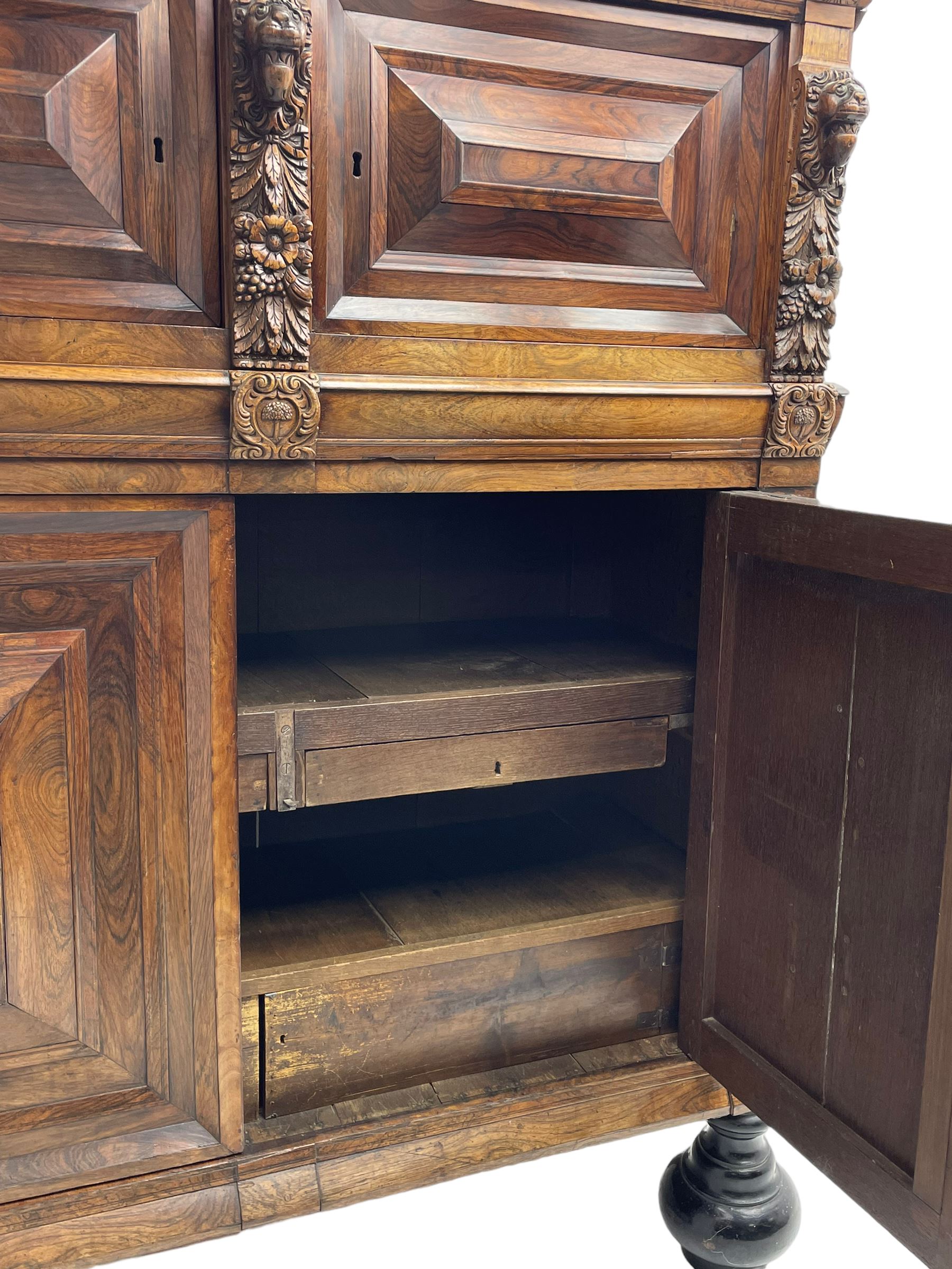 Late 17th century Flemish/Dutch rosewood and oak ‘Zeeuwse Kast’ or cupboard, projecting cornice carved with three putti masks, the uprights carved with lion masks over ribbons, flower heads and foliage, enclosed by four geometric panelled doors, lower central upright carved with flower head over foliate ribbon with bird among foliage, the escutcheon hidden by swivel berry carved cover, interior fitted with shelves, two drawers and shallow hinged cupboard, on two large turned and ebonised feet, circa 1680