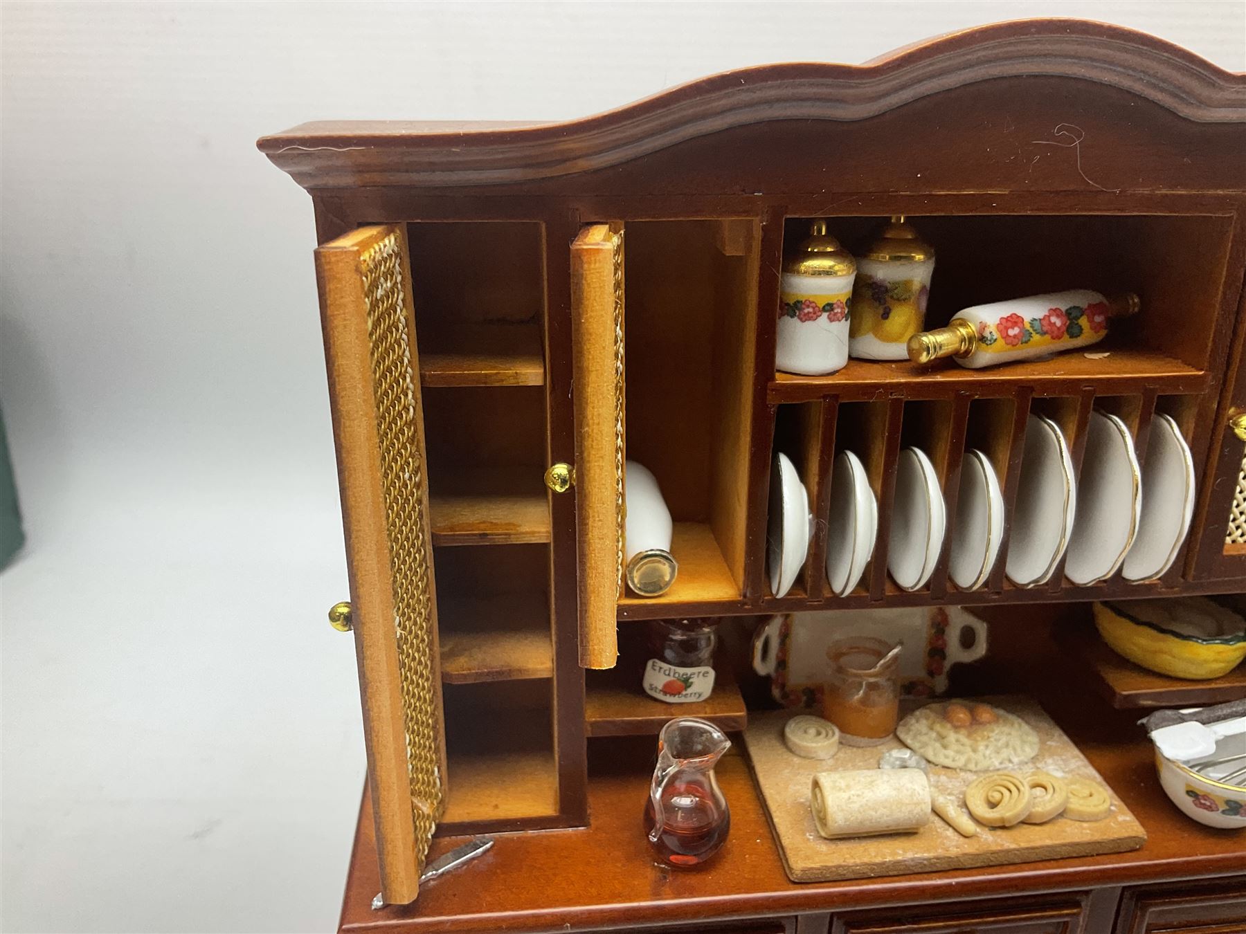Collection of kitchen and bedroom dolls house furniture, to include two units housing Reutter, Germany ceramic plates, tea wares and accessors comprising one example with a Belfast sink with various pots and pans and jars, the second housing various baking equipment, two dressers, baking table, shelf unit housing various jars of herbs and basket of produce, fridge, and lace and jacquard bedroom suite including bed, pair of bedside tables, dressing table and ottoman