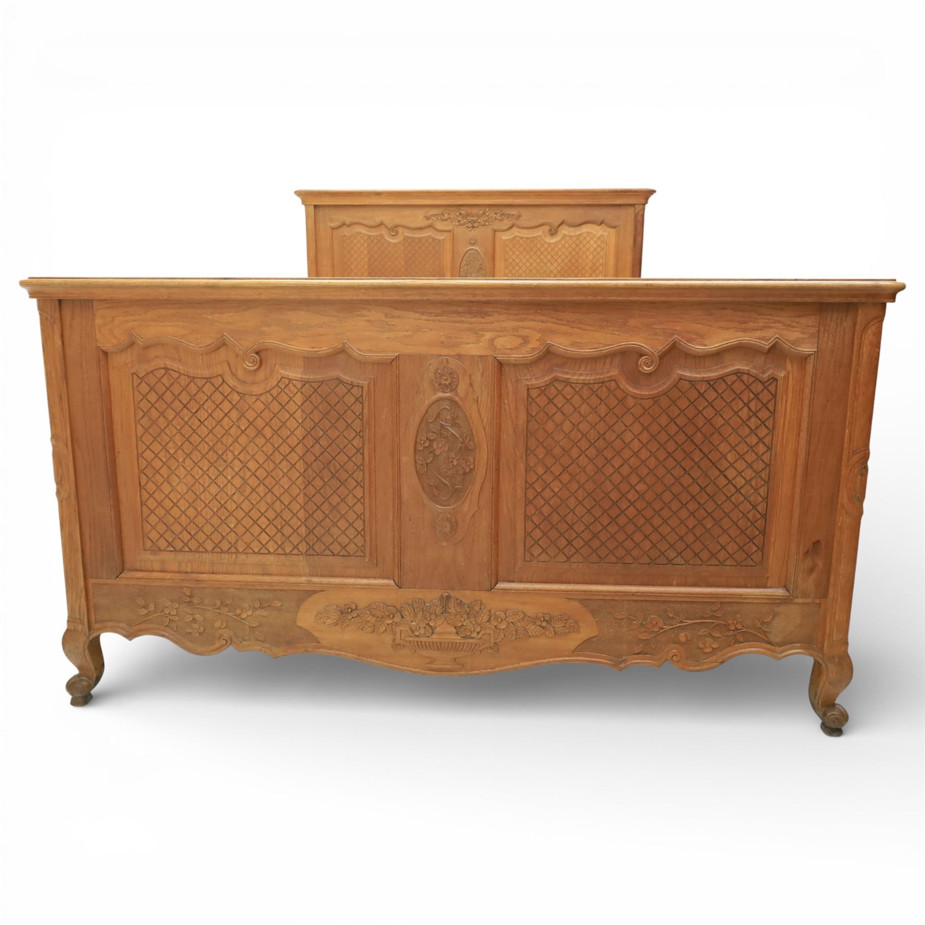 Early 20th century French oak double bedstead, the shaped and moulded headboard carved with central floral cartouche and scrolling foliage above lattice carved panels, the conforming footboard with pierced and carved decoration, shaped apron with foliate carving, raised upon cabriole supports