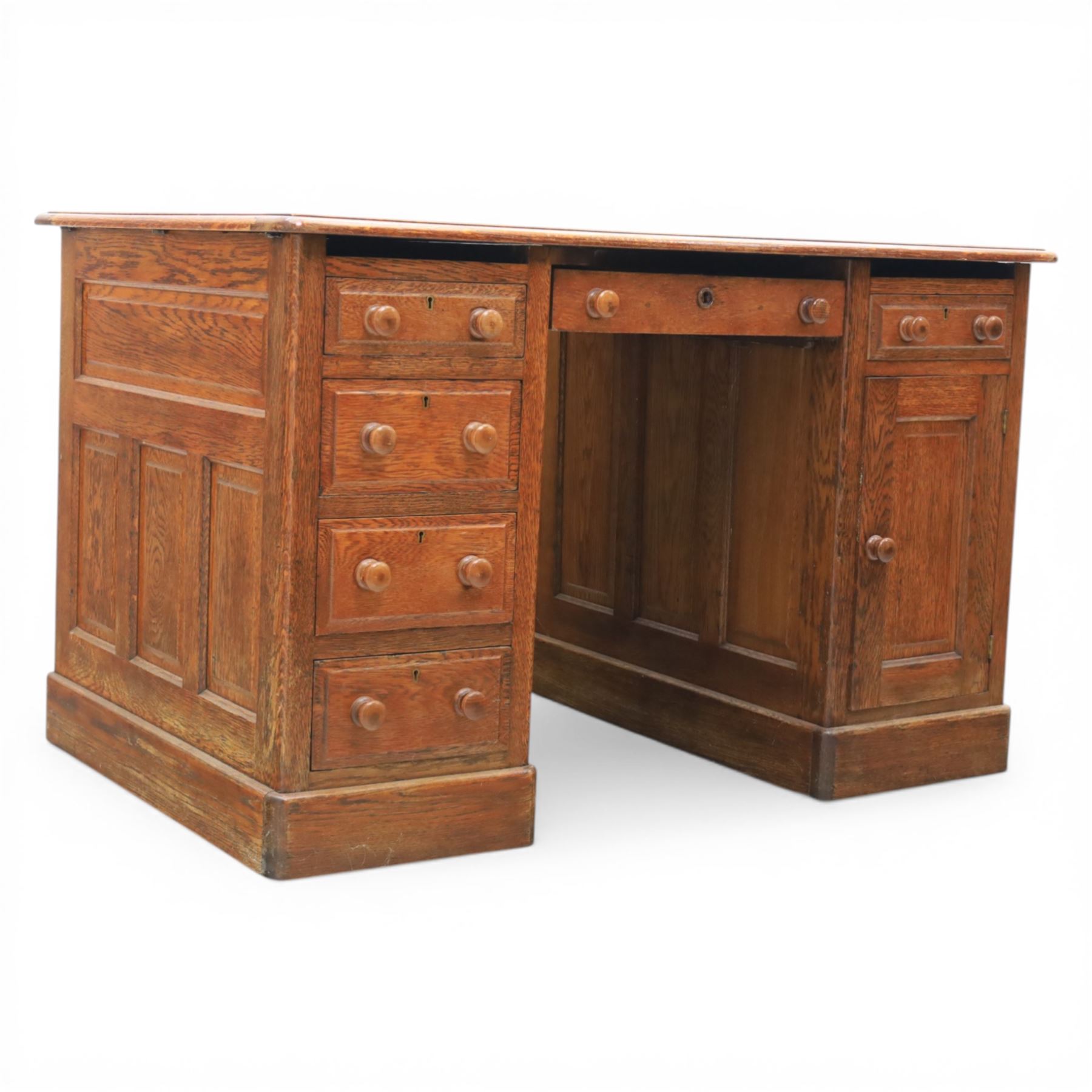 20th century oak compact pedestal desk, tooled green leather inset top, above a single frieze drawer, with a bank of four graduated drawers and a drawer and cupboard, panelled sides raised on castors