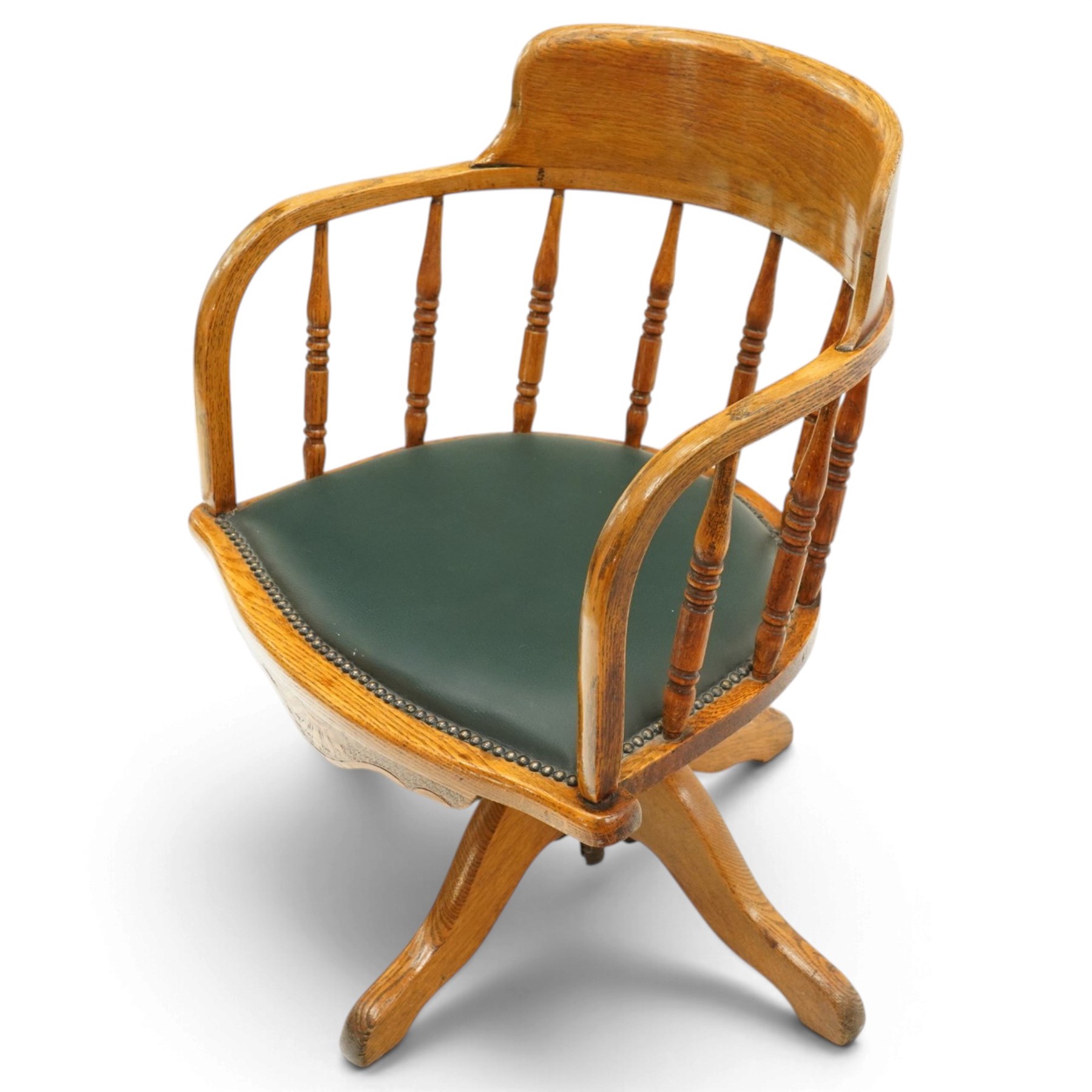 Edwardian oak captains swivel desk chair of tub form, shaped cresting rail over spindle supports and green-leather upholstered seat, foliate apron over swivel action and four-spoke base