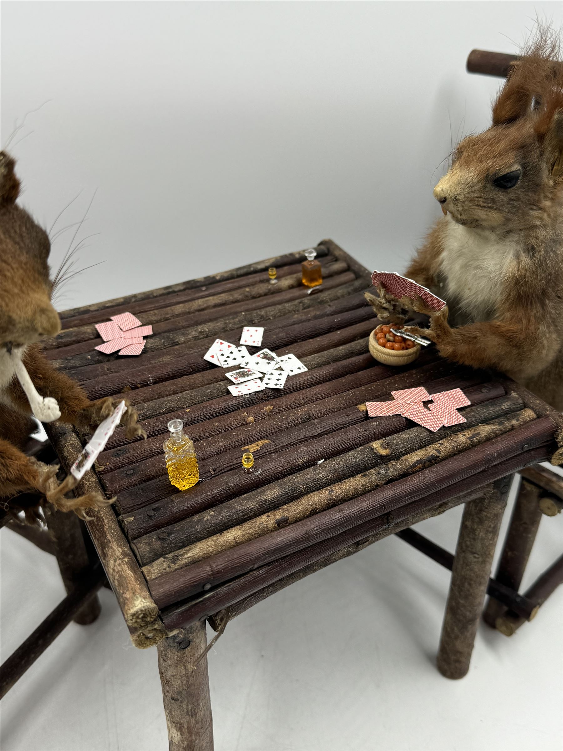 Anthropomorphic Taxidermy: Two red squirrels (Sciurus vulgaris), both seated upon a chair holding playing cards, one smoking a pipe 
