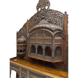 Late 19th century Indian Burmese carved and pierced hardwood and brass inlaid wall shelf, the shaped back profusely decorated with trailing and interlaced foliage, with projecting architectural structures, the central balcony with canopy top and five open windows with arched apertures on columns, two flanking five-sided balconies, the shelf supported by six foliate carved columns with pierced cusped pointed arches 