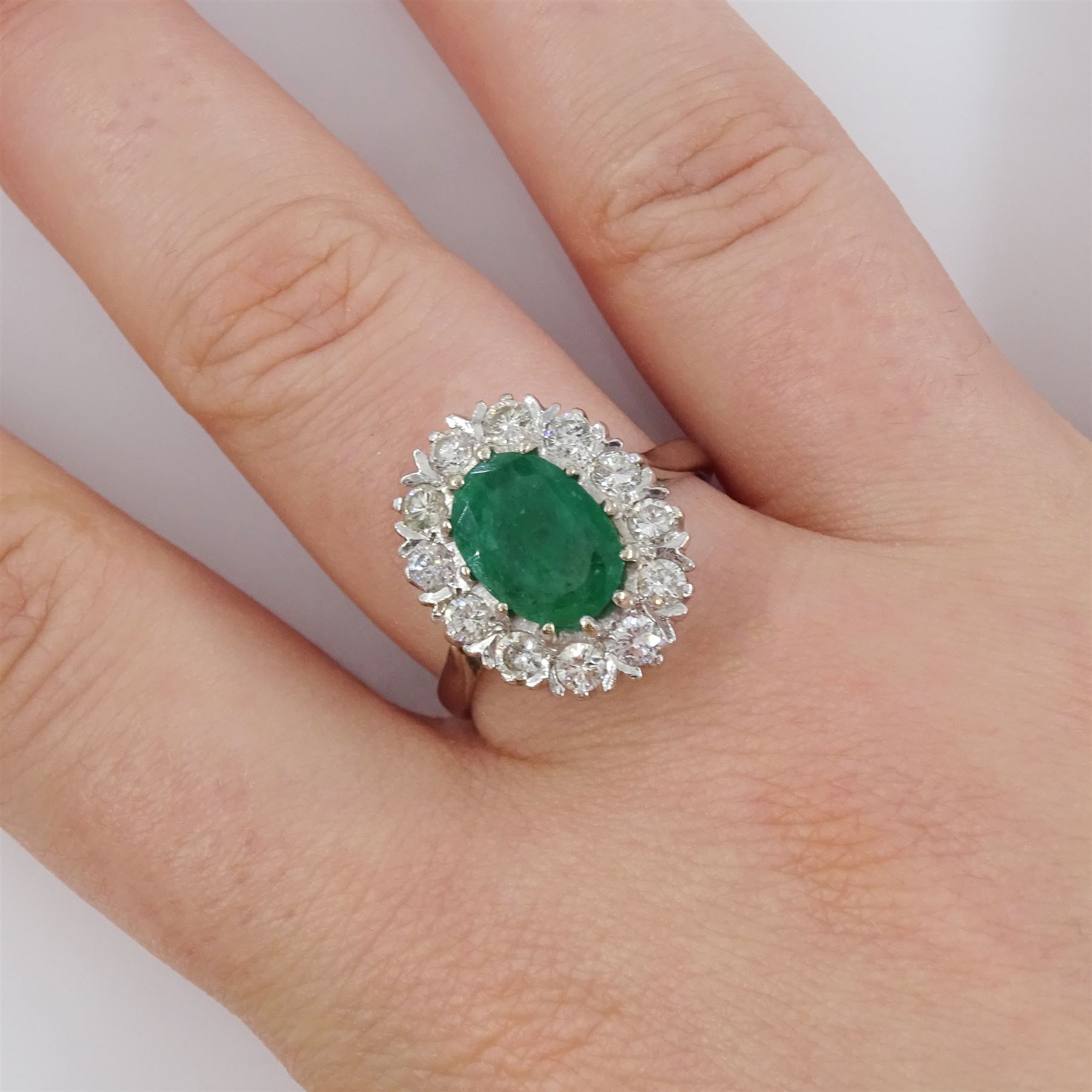 White gold emerald and diamond cluster ring, single oval cut emerald of approx 1.35 carat, surrounded by twelve brilliant cut diamonds, stamped 18ct, total diamond weight approx 0.85 carat