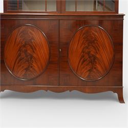 William Tillman - Early 20th century mahogany display cabinet, moulded cornice above a frieze carved with roundels and fluting, pair of astragal glazed doors enclosing adjustable shelving, the lower section fitted with twin panelled cupboard doors centred with oval veneered panels, shaped apron and bracket feet